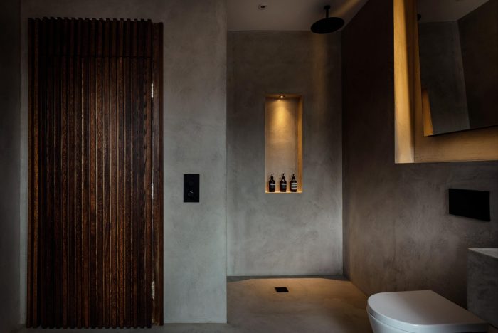 Shower with shower niche and beige stone textured walls with a wooden panelled door to the left