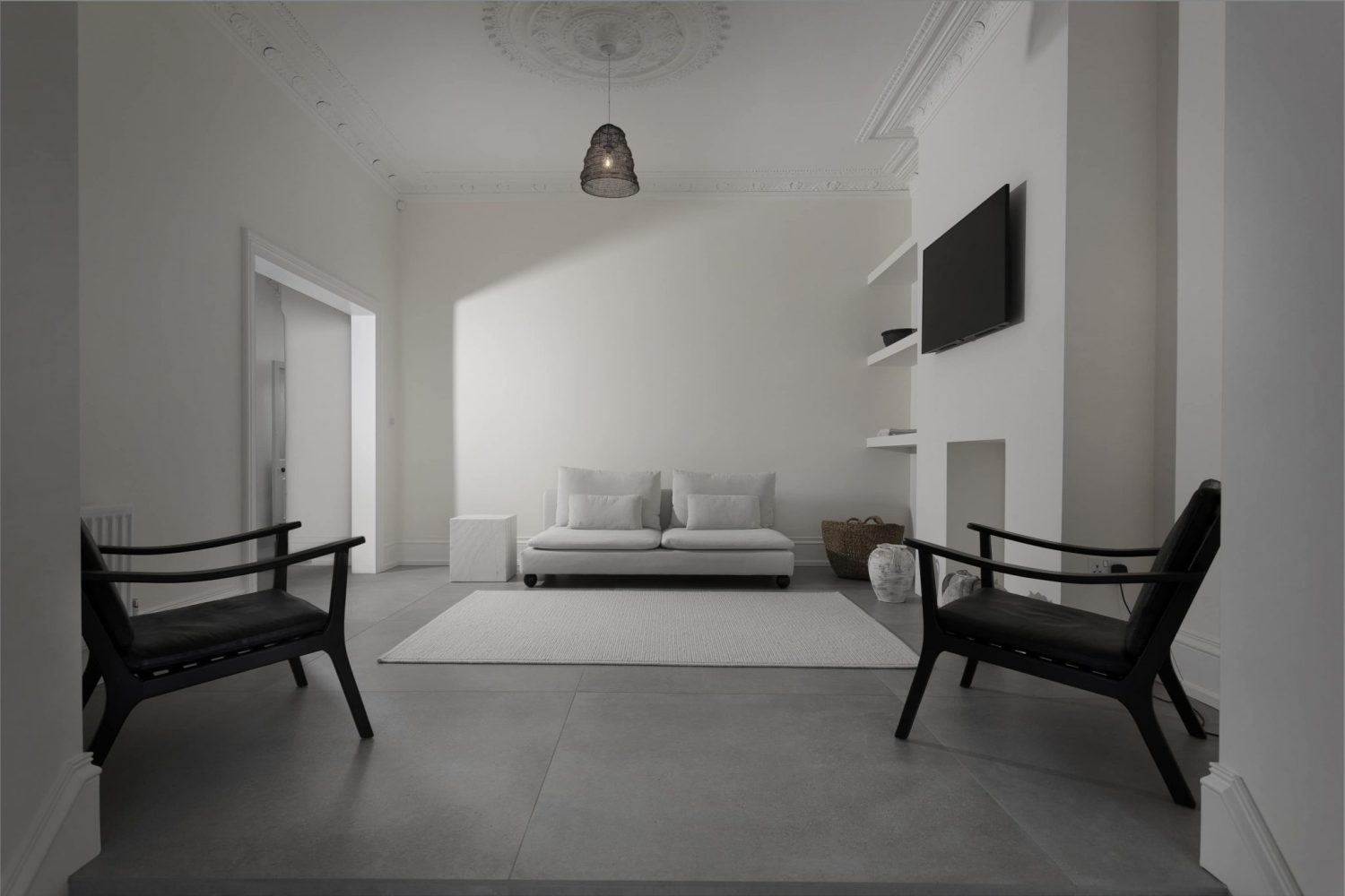 White living room with white sofa and rug on grey tiled floor with black chairs on either side