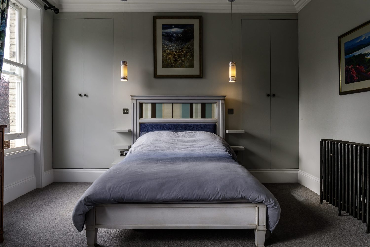 Bedroom with muted blue bedsheets and pendant lights hanging beside