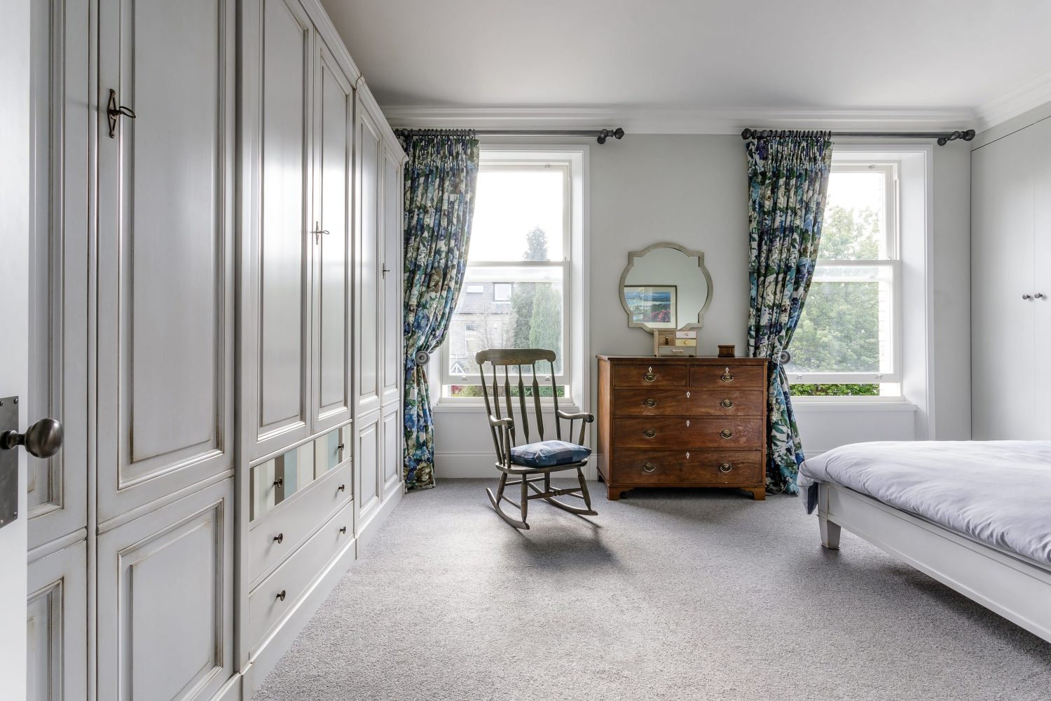 Rocking chair in bedroom with antique wooden drawers and white wardrobes