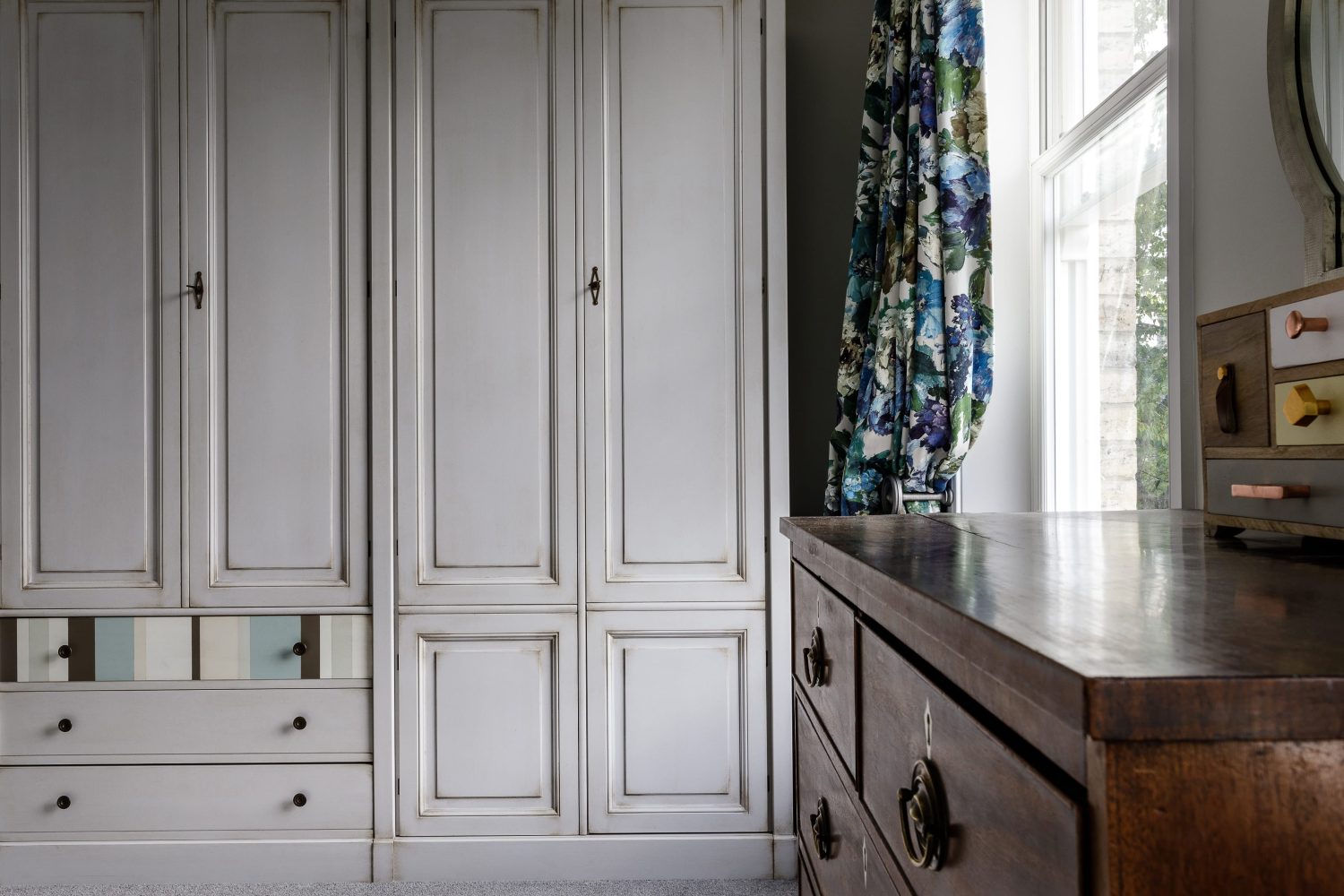 Antique white wardrobes beside blue and purple floral curtains