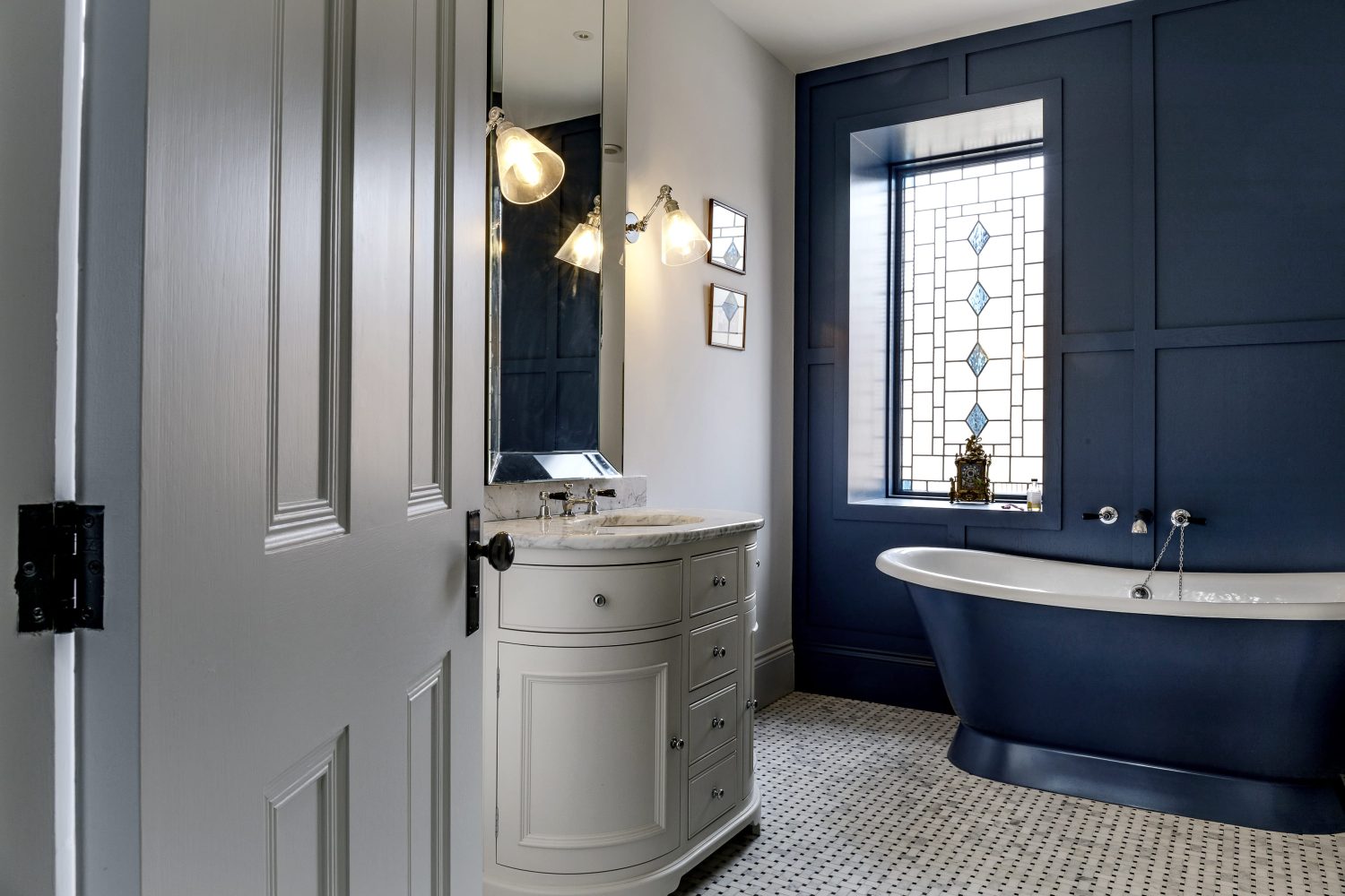 Dark blue bath beside dark blue wall with white sink and stained glass window