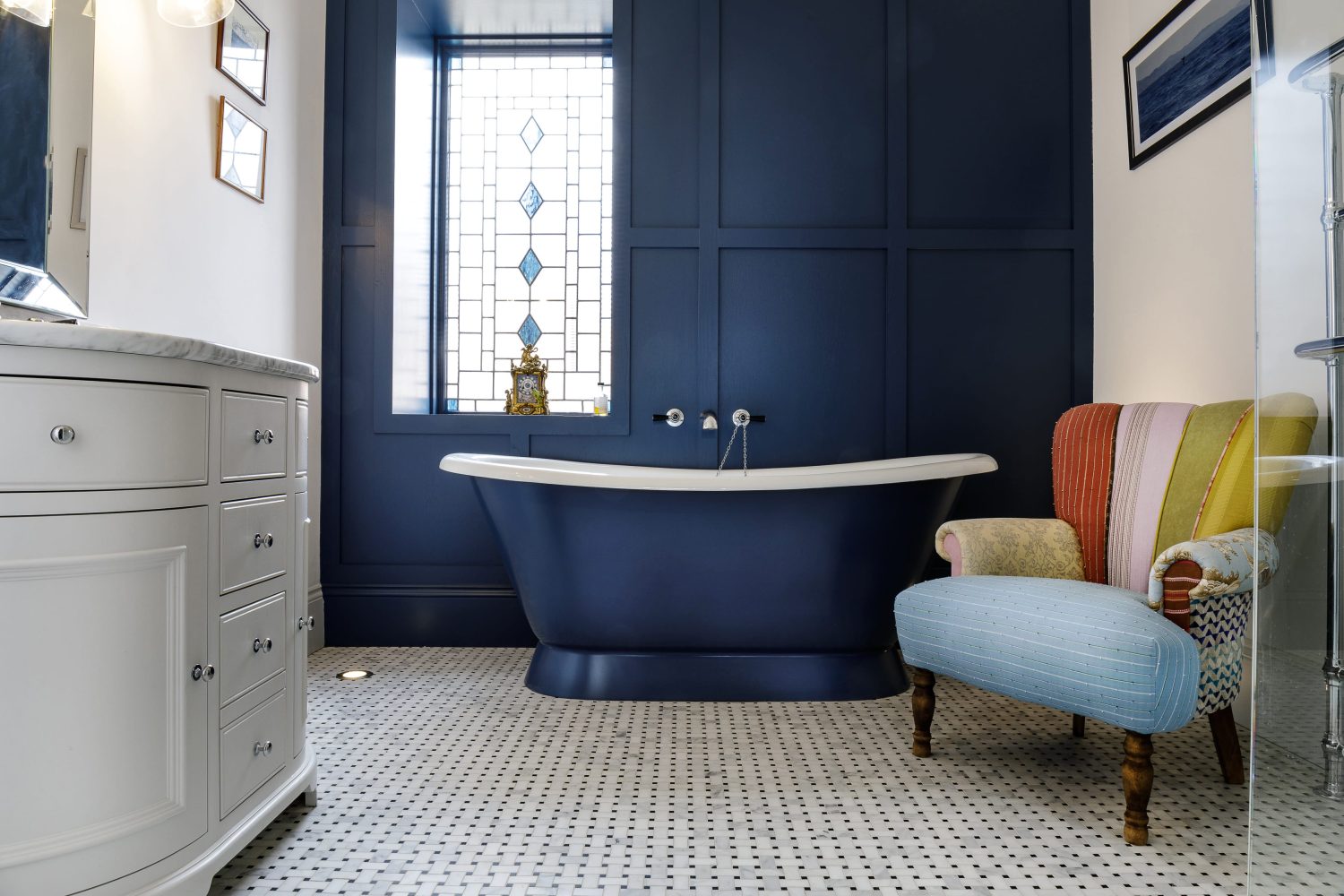 Dark blue bath and wall of same colour with multi-colour striped chair beside