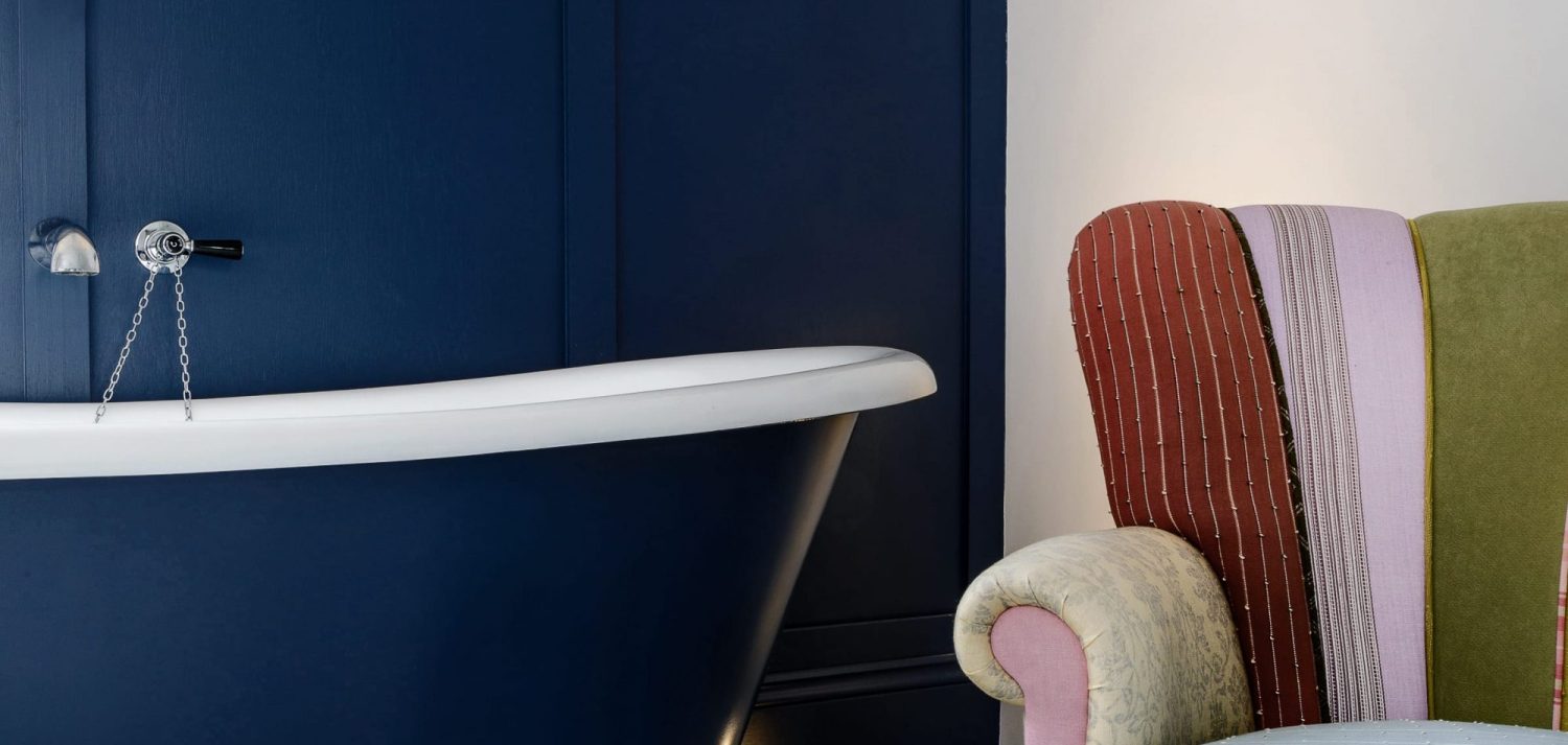 Close up corner of dark blue bath with multi-colour striped chair beside