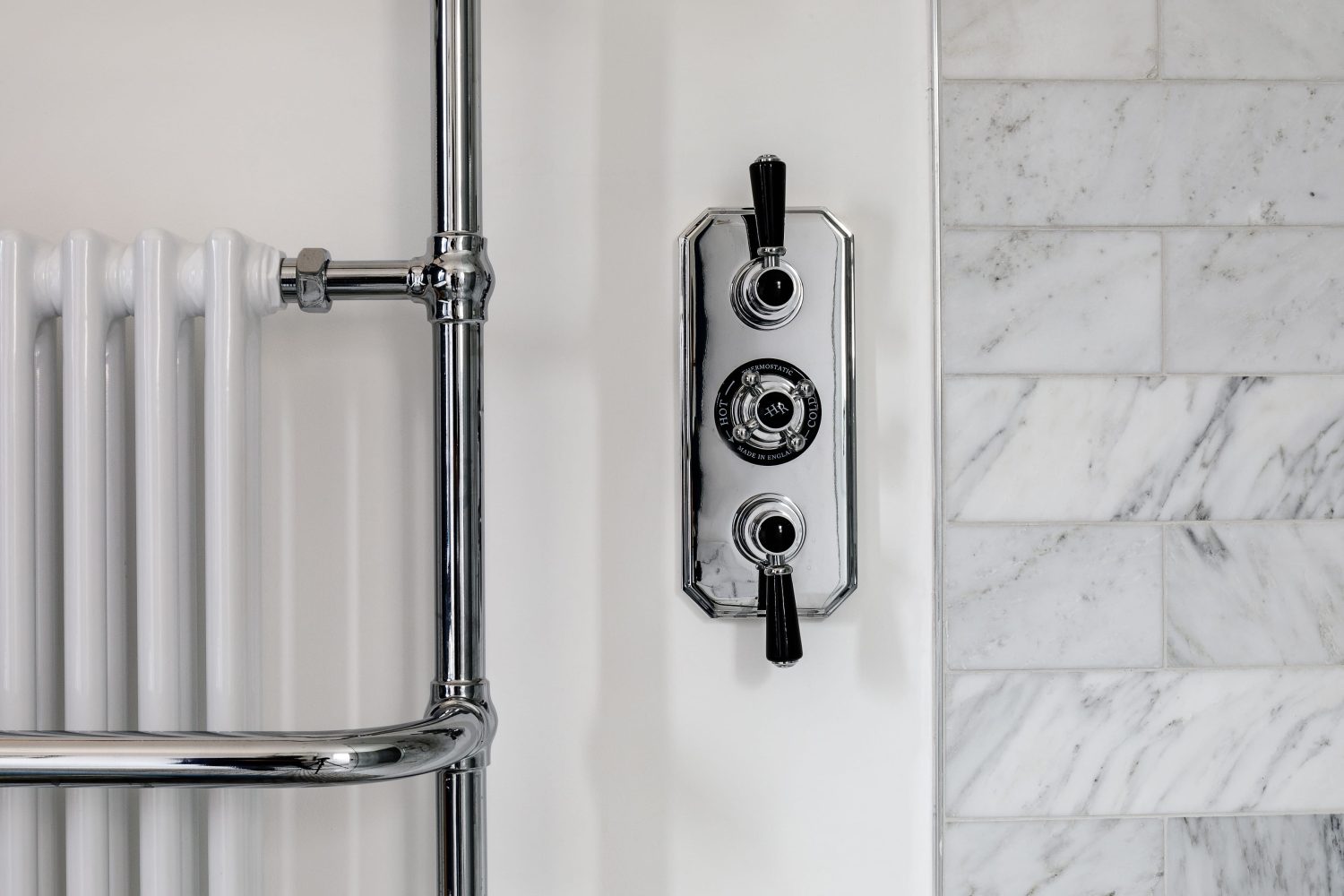 Close up chrome shower tap with black accents beside marble tiles and radiator