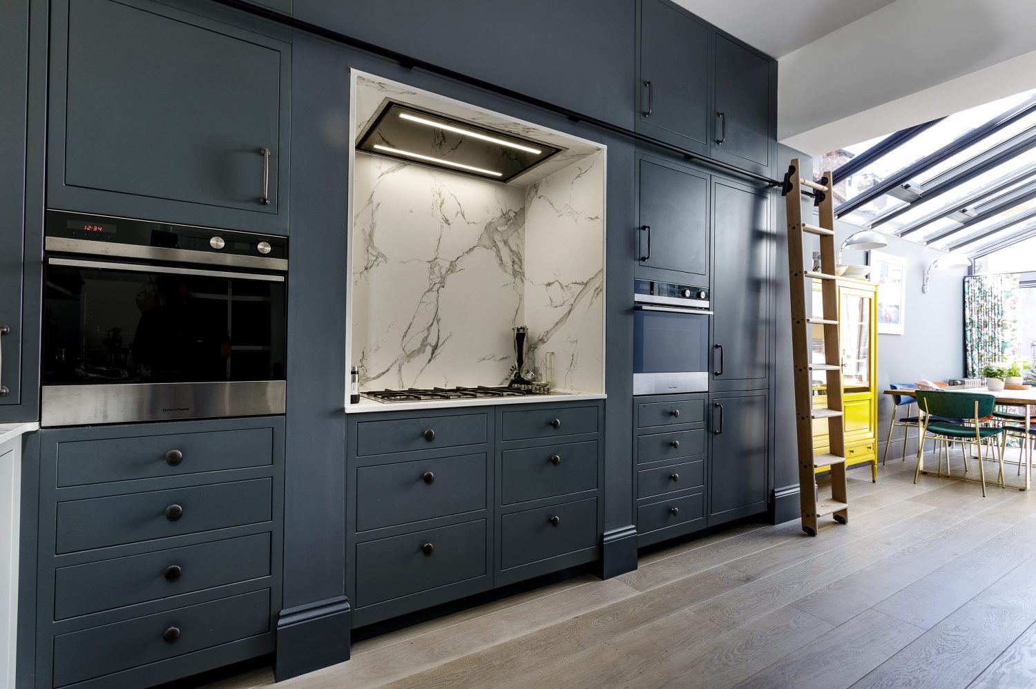 Dark blue kitchen with wooden sliding ladder and white marble stove area