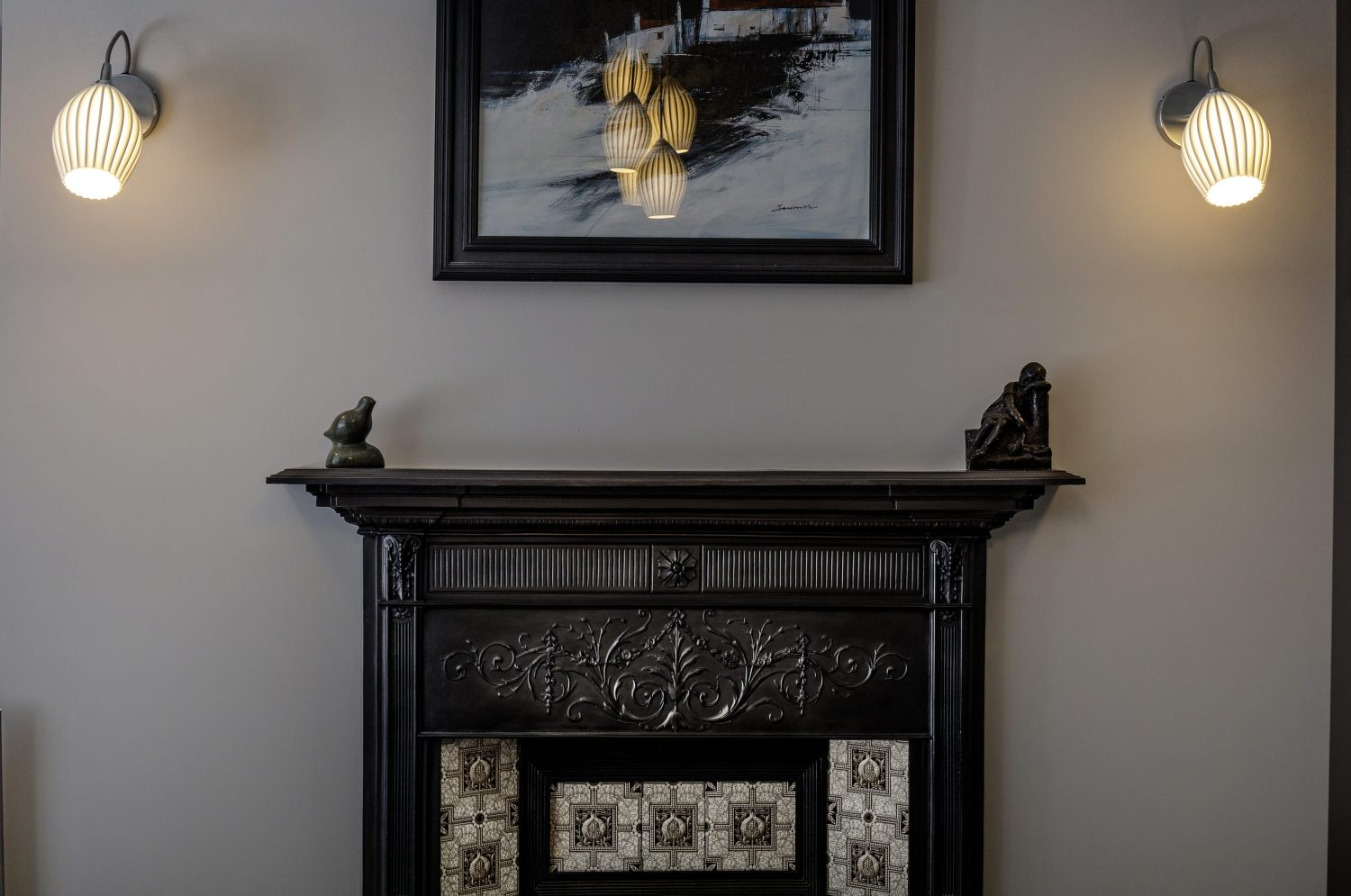 Black ornate fireplace with black framed artwork above surrounded by two wall lamps