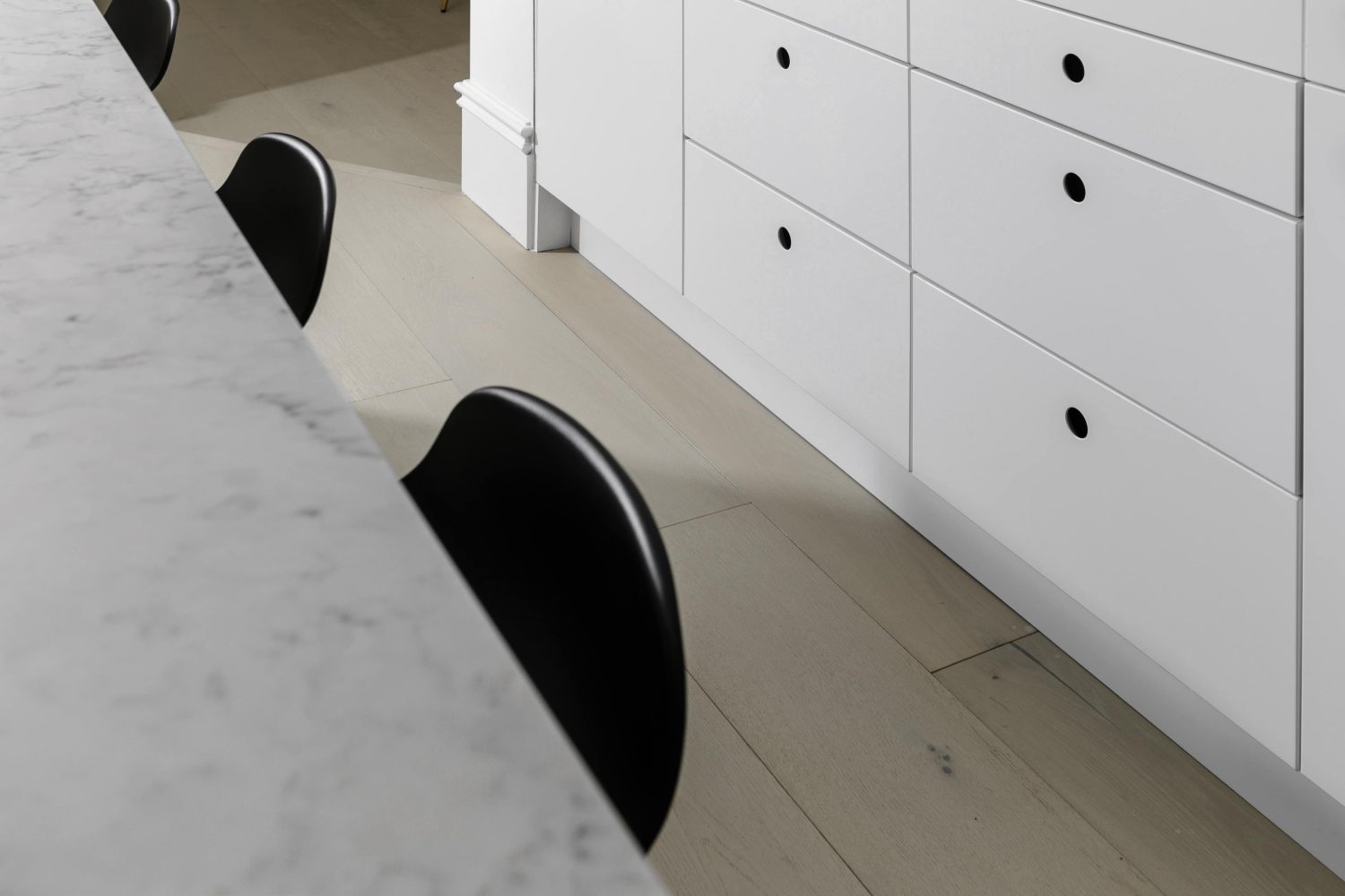 Close up white marble countertop with black barstools beside and white drawers with circular cut-out handles