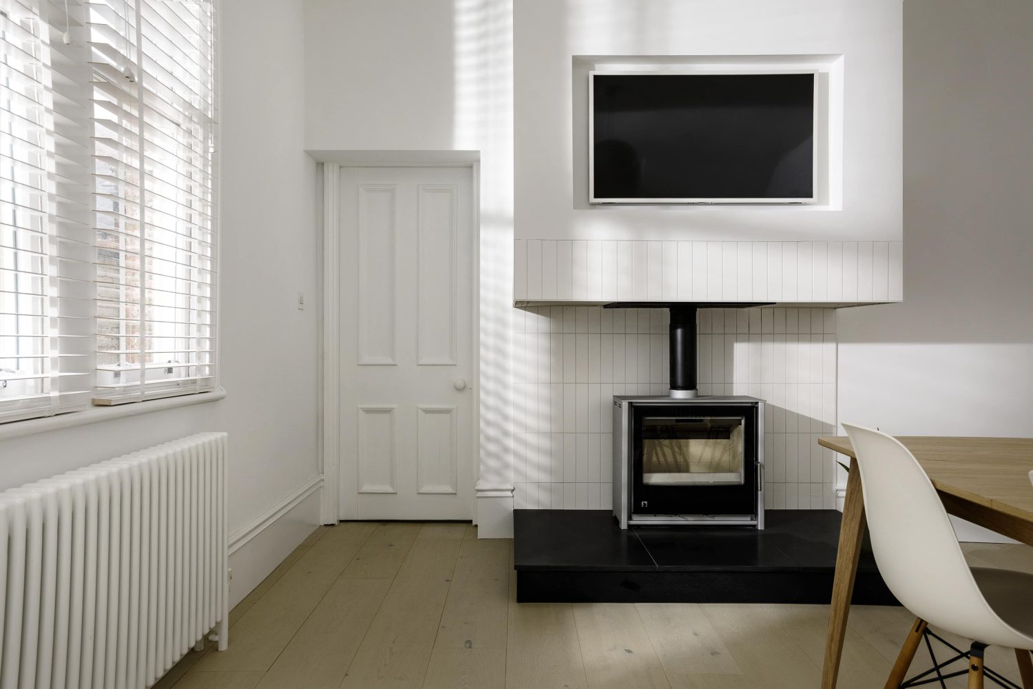 TV on a white wall above a black log burner with a white door to the left