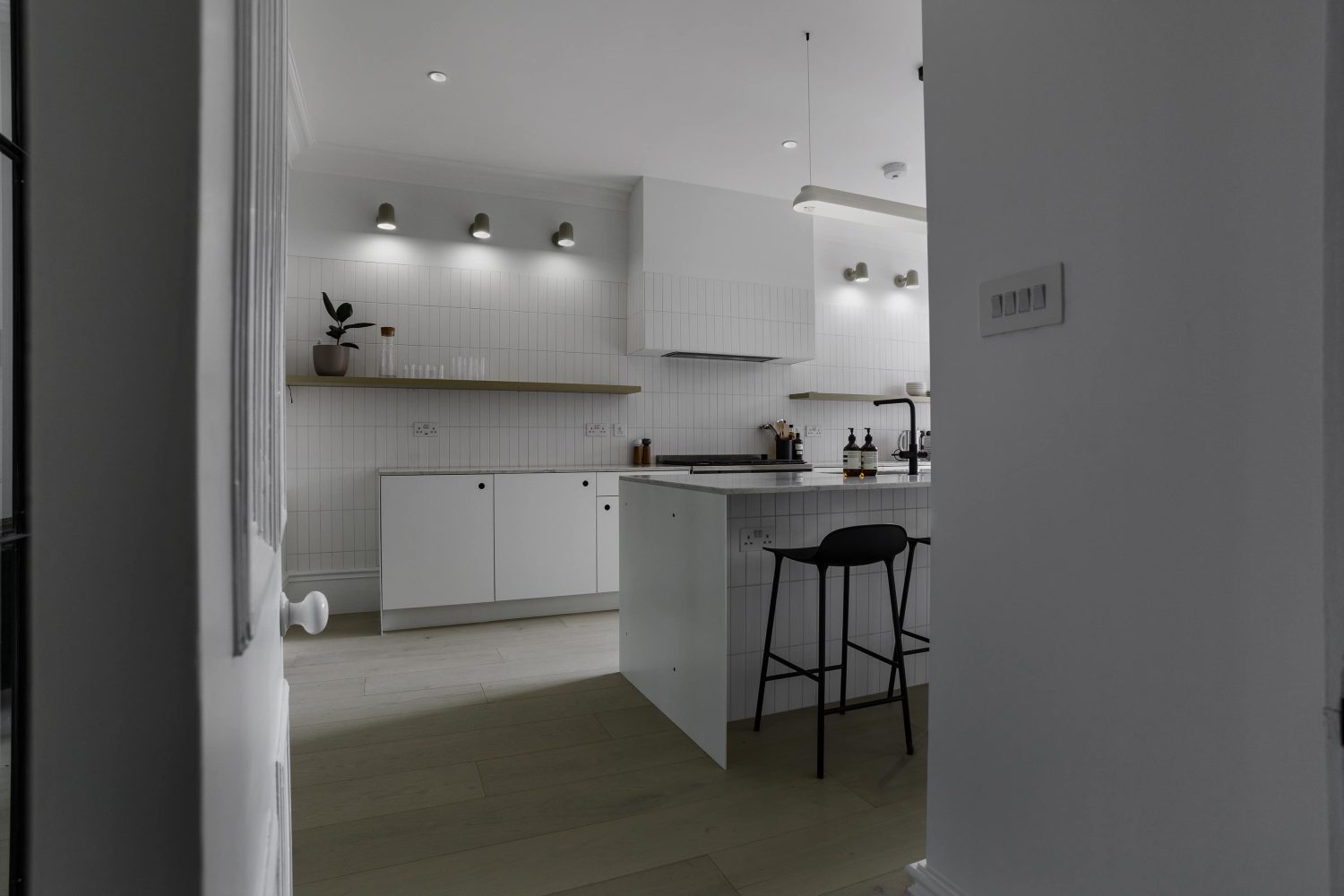 Kitchen with white tiled walls and island in the centre with black barstools