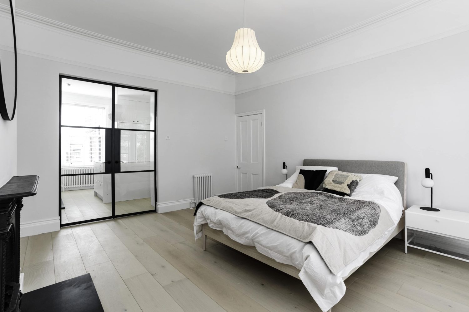 Bedroom with white walls and Crittall-style double doors. Double bed in the centre with pendant light hanging above