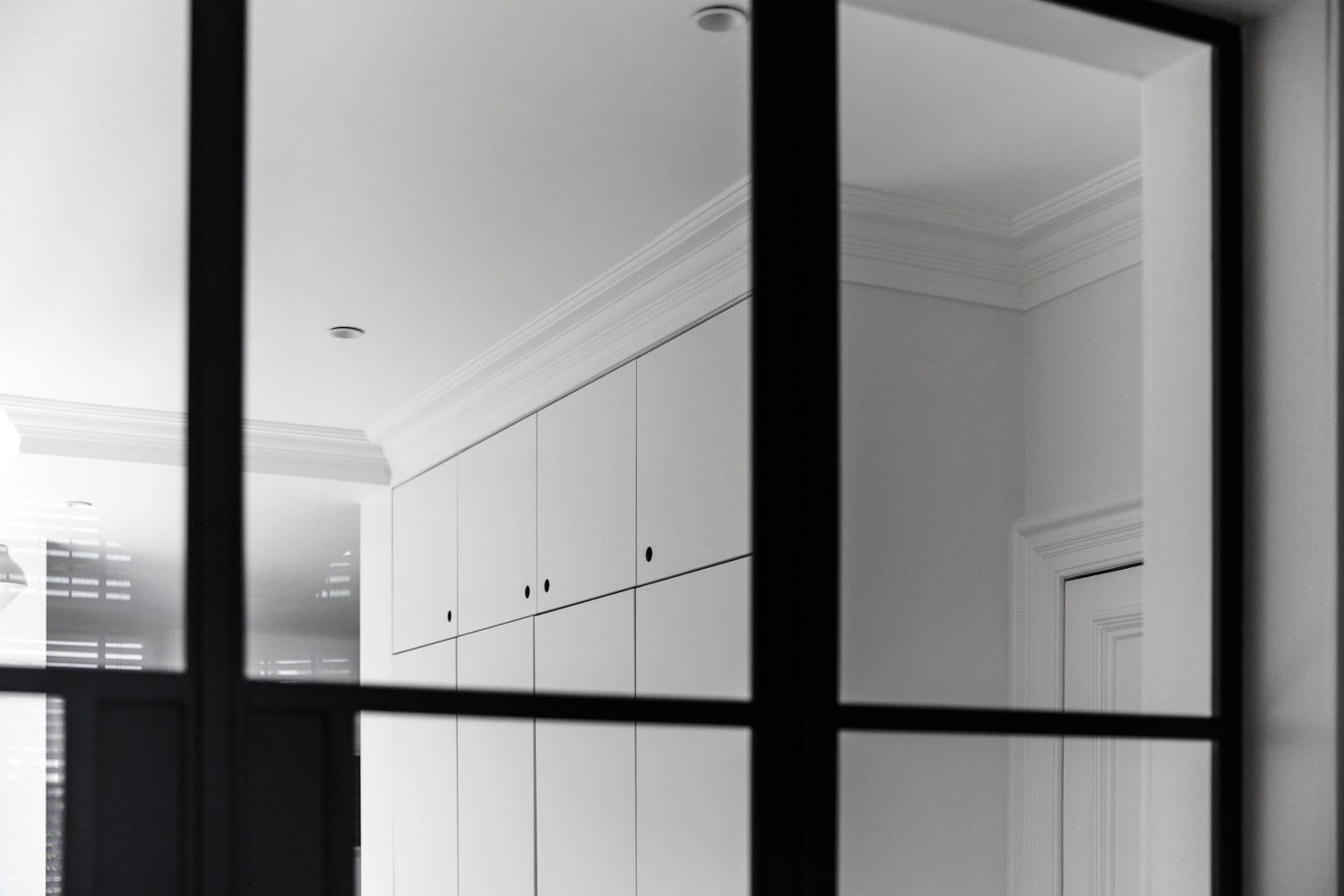 View through Crittall-style doors to room with white built-in cupboards with circular cut-out handles