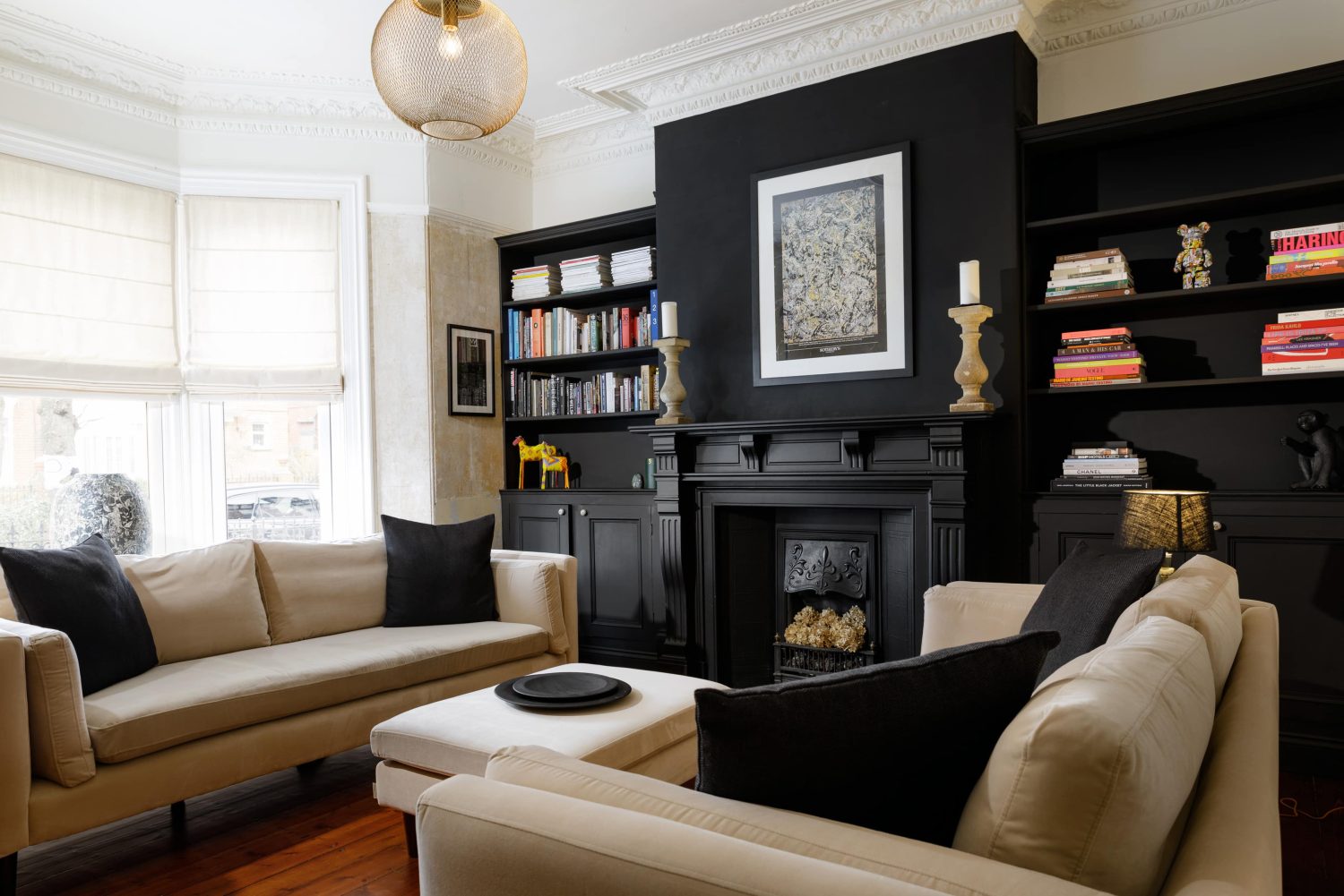 Living room with two beige sofas beside a black wall with a black fireplace and black shelving on either side holding books and ornaments