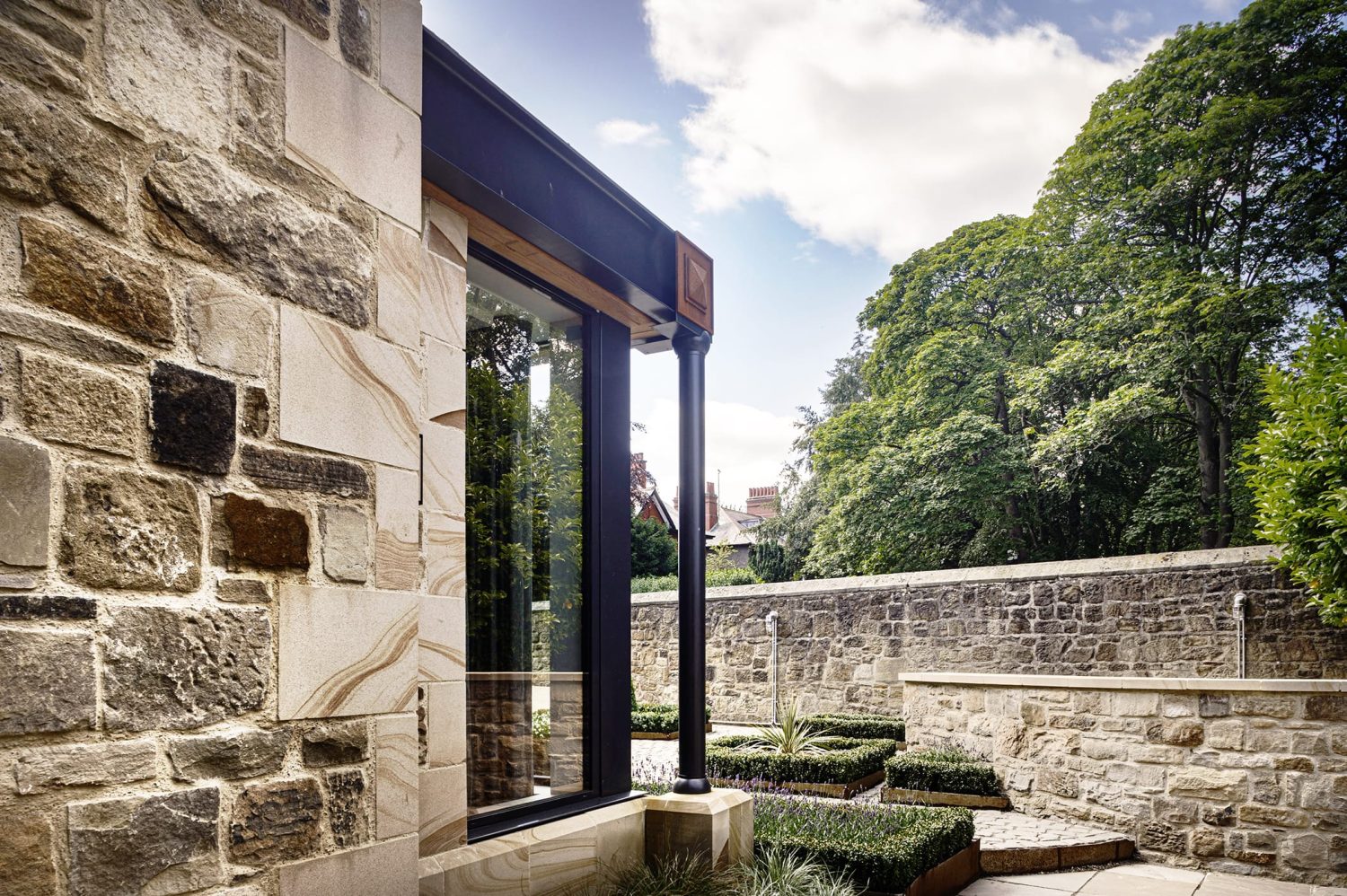 Exterior corner of stone built house with black framed window with copper accents in corner