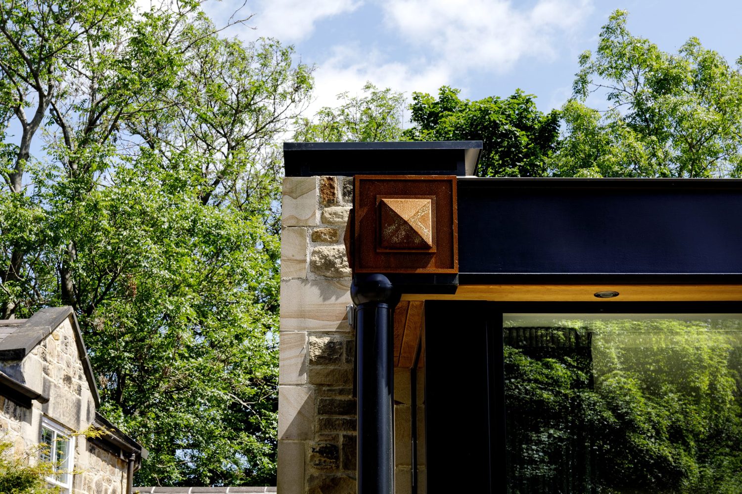 Exterior corner of stone built house with black framed windows with square copper accents in corner