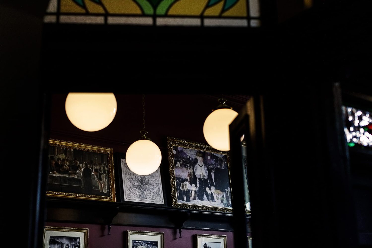 Doorway looking through to framed photos on a dark red wall with sphere pendant lamps hanging in front
