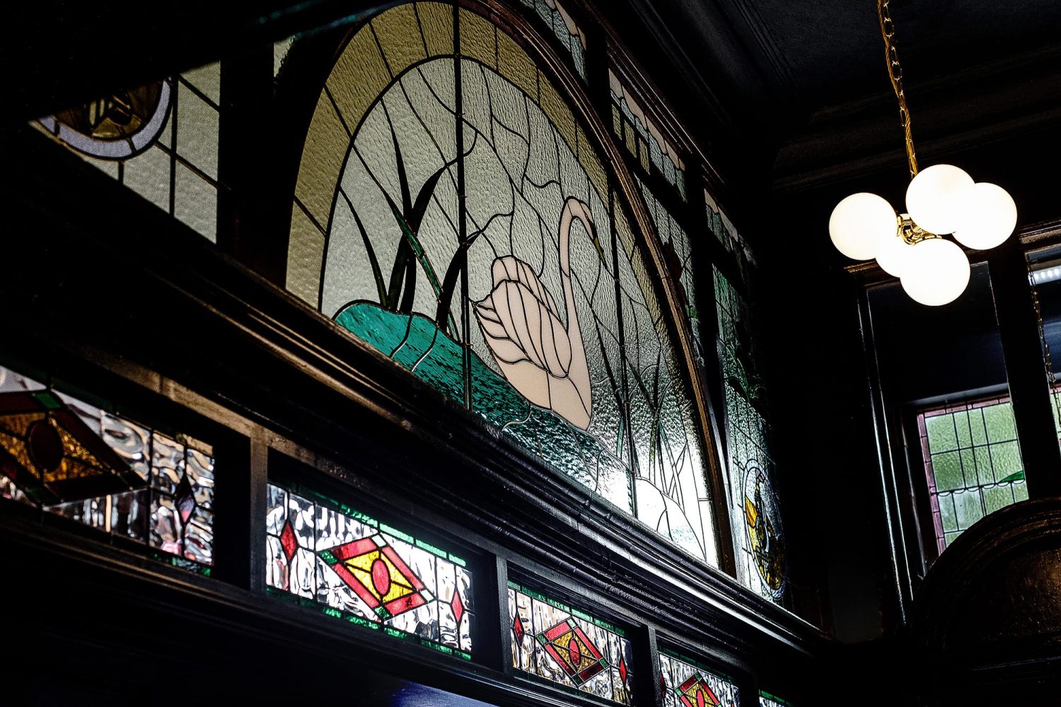 Large stained glass window featuring image of a swan with a pendant light hanging to the right