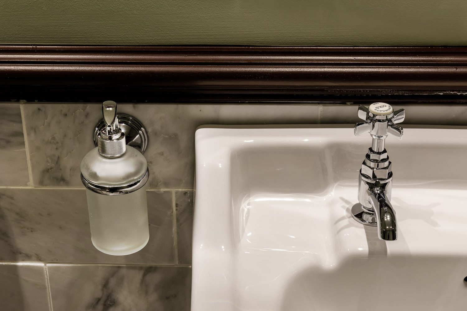 Corner of white sink with chrome tap and soap dispenser attached to tiled wall on the left