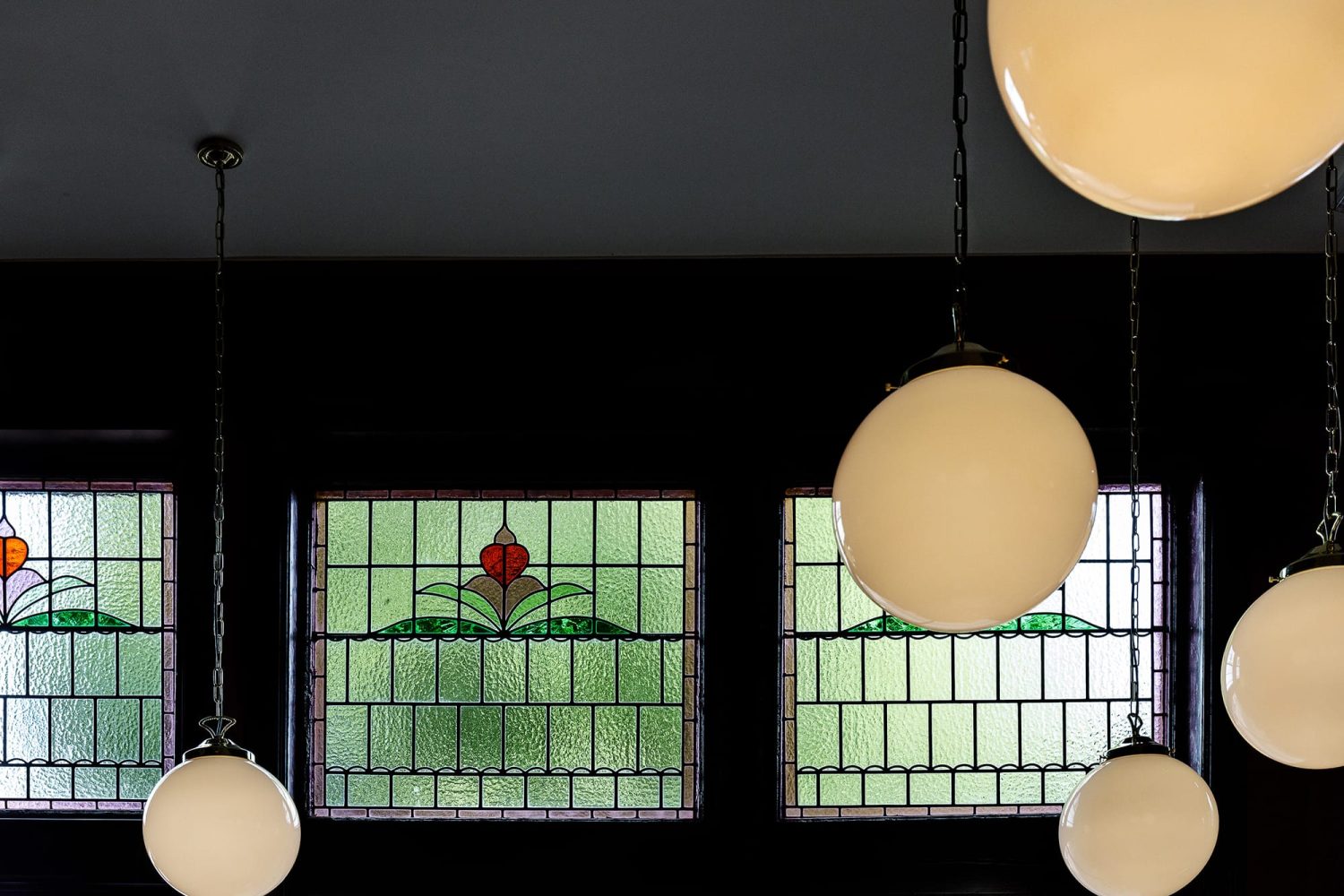 Multiple sphere pendant lights hanging from ceiling with stained glass windows behind