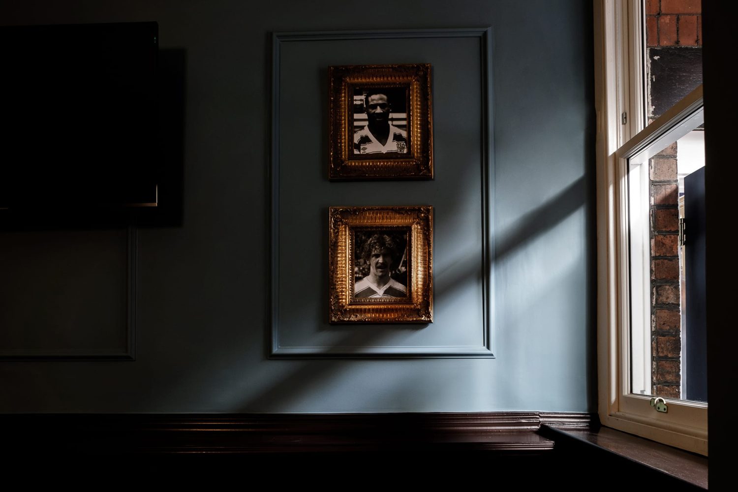 Gold framed portraits on a muted blue wall with light shining through window to the right