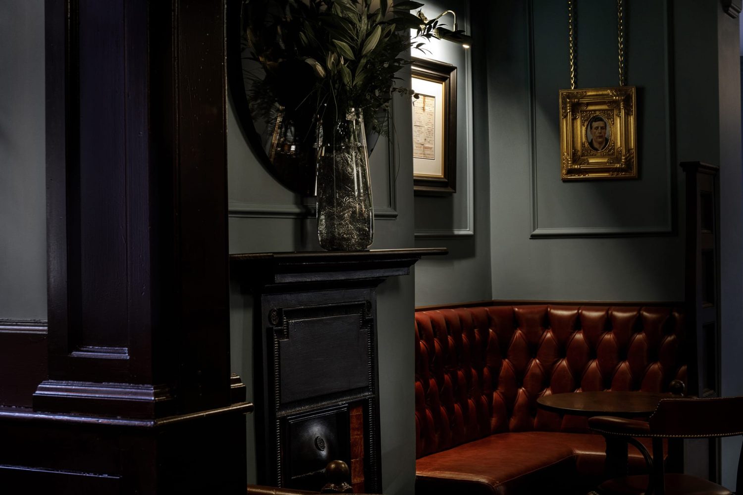 Dark red corner booth seat with gold framed photo hanging above and a small black fireplace to the left
