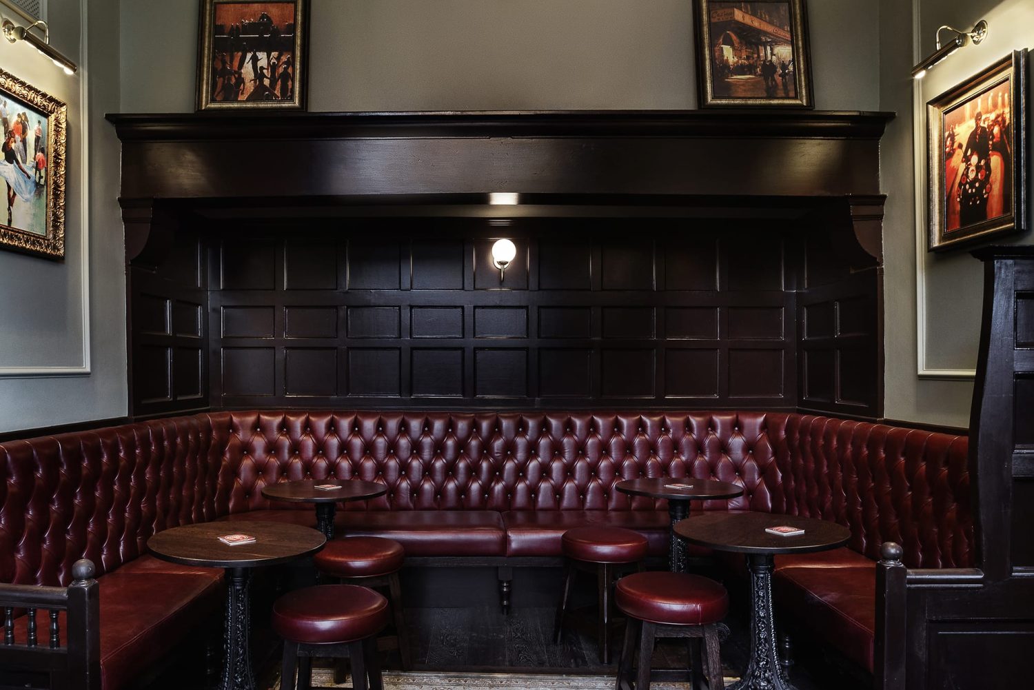 Dark red booth seating with dark brown panelling on wall behind and four small circular tables with stools