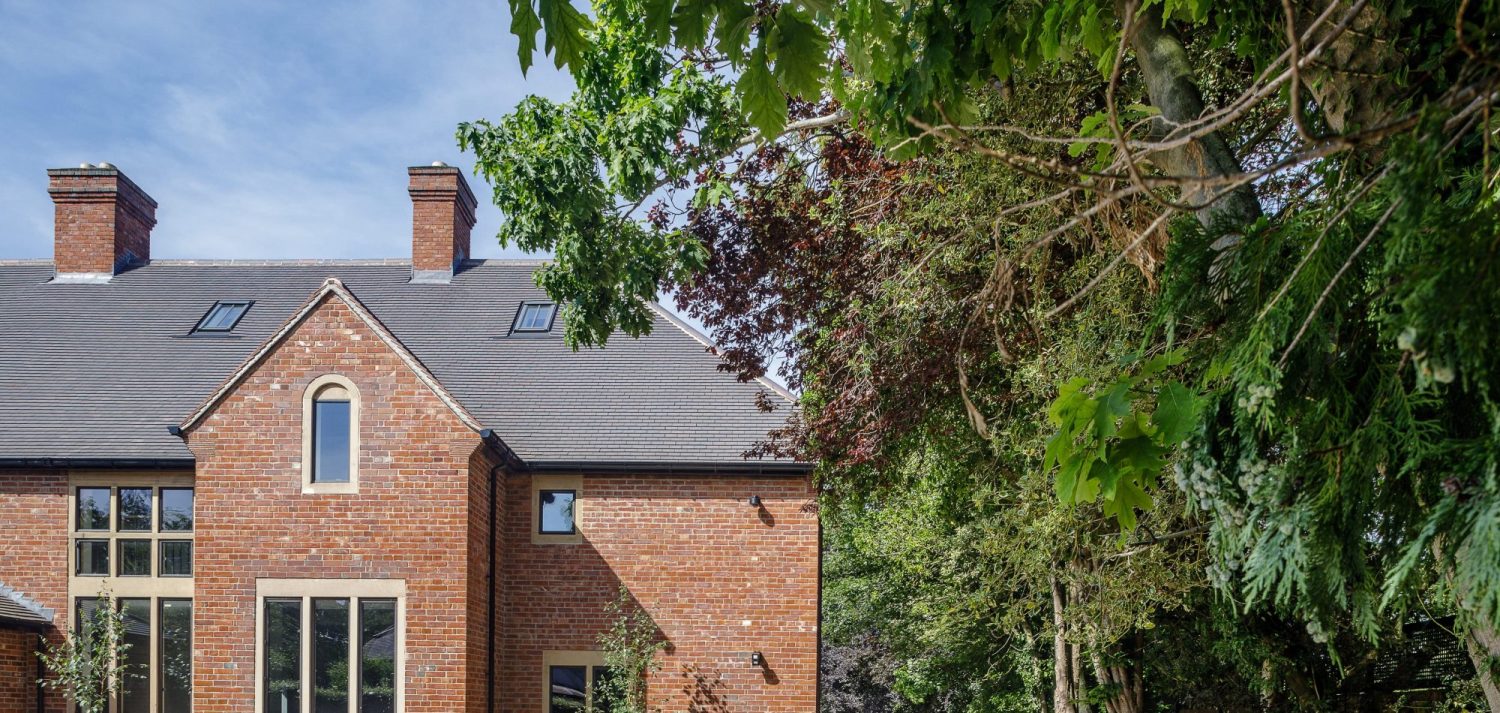 Exterior corner of house with brick walls and slate roof with trees to the right