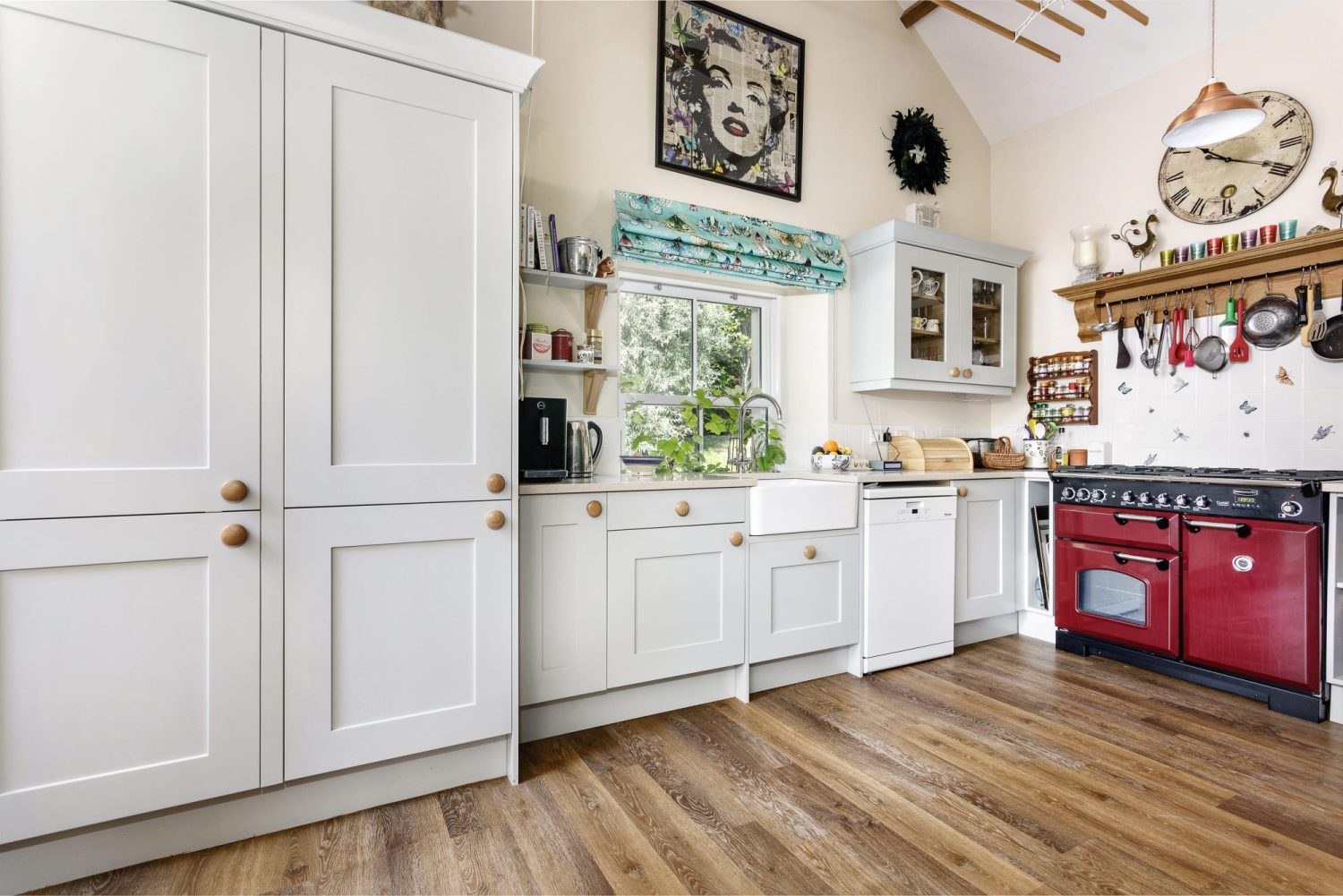 Cottage kitchen with light grey cabinetry and deep red cooker unit with eclectic wall decorations