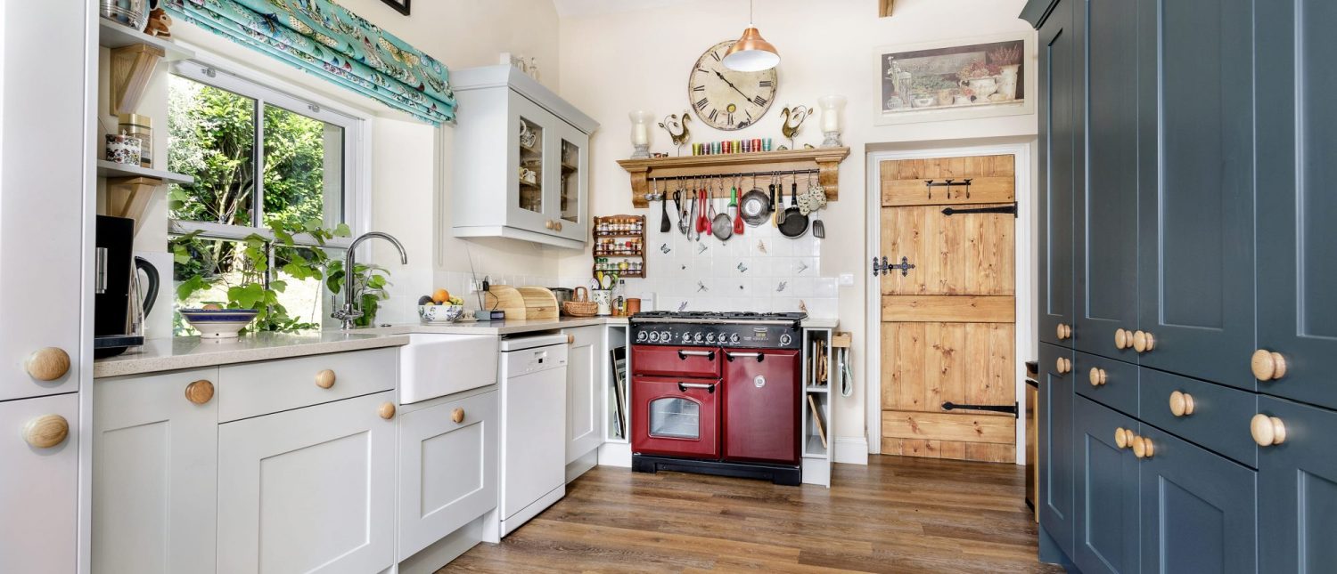 Cottage kitchen with light grey and dark blue cabinetry surrounding deep red cooker unit and wooden door