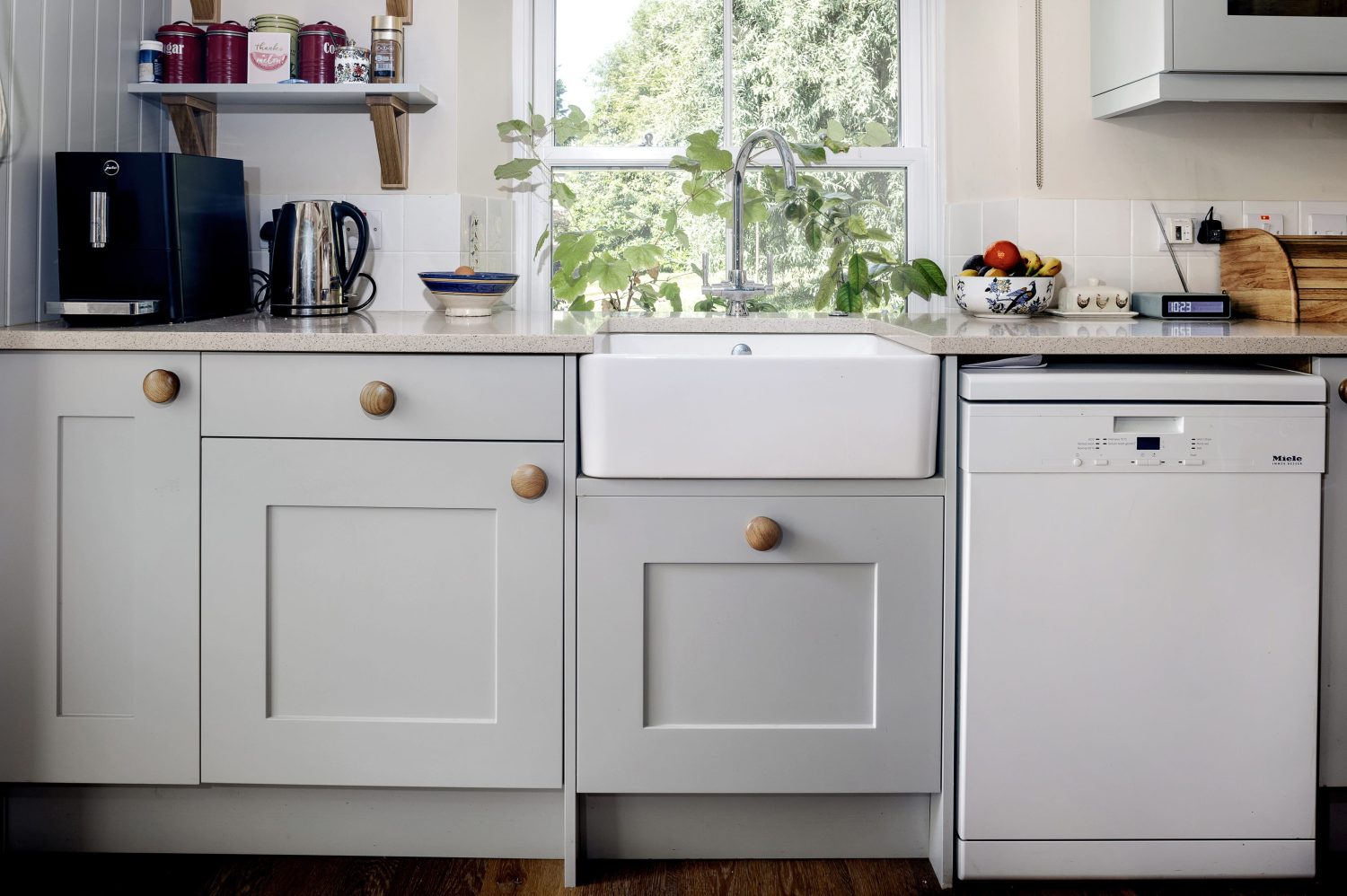Cottage kitchen sink area with light grey cabinetry surrounding and white dishwasher