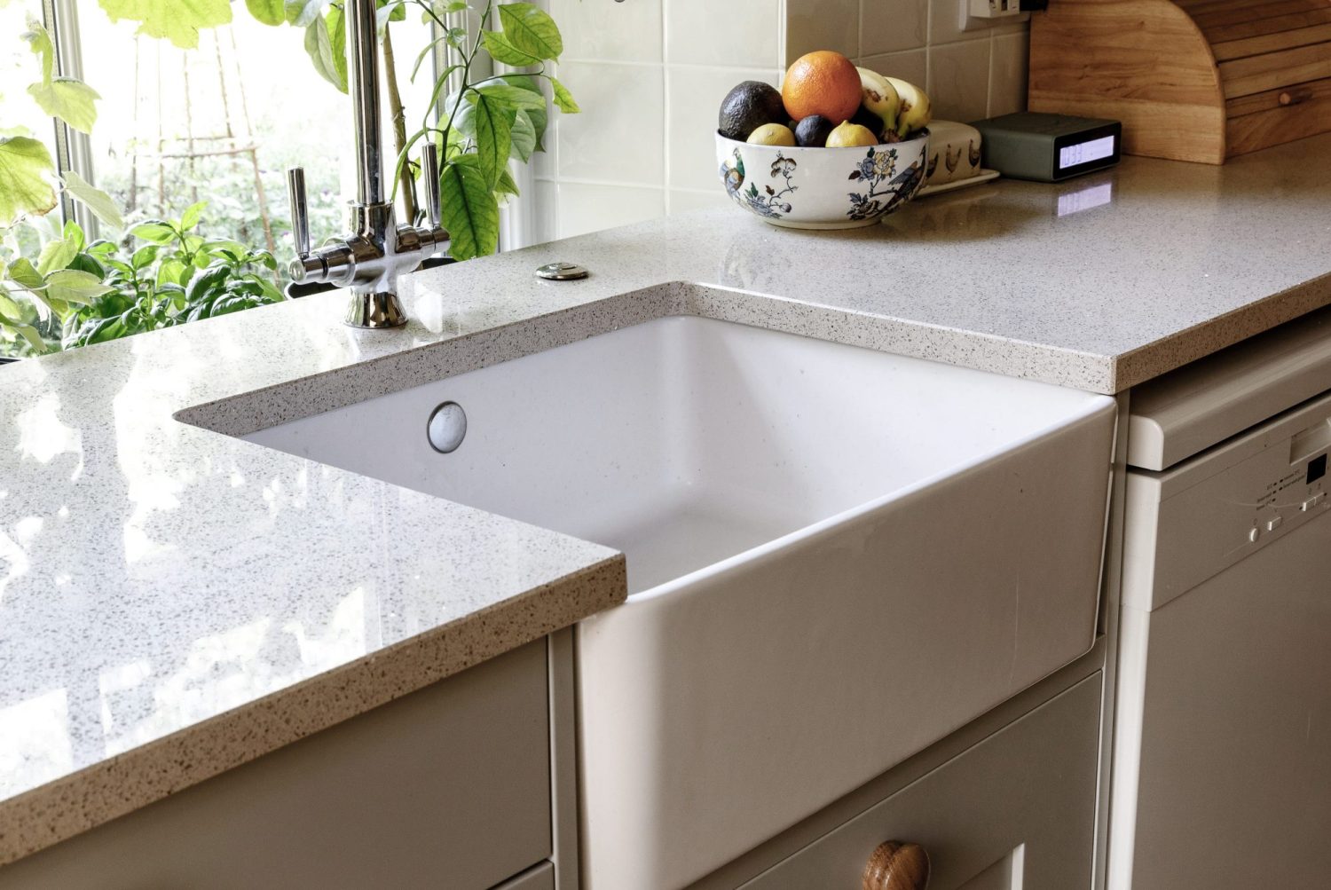 Close up on white sink with white speckled countertops and fruit bowl