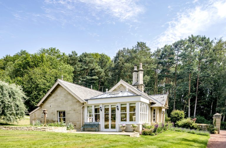 Exterior of cottage side view with white conservatory extension and trees surrounding