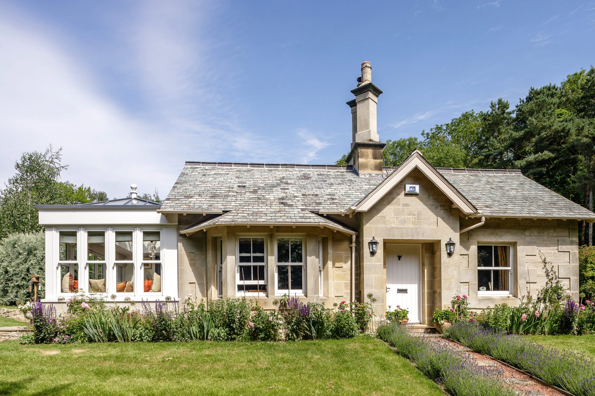 Exterior front of stone built cottage with chimney and white conservatory extension