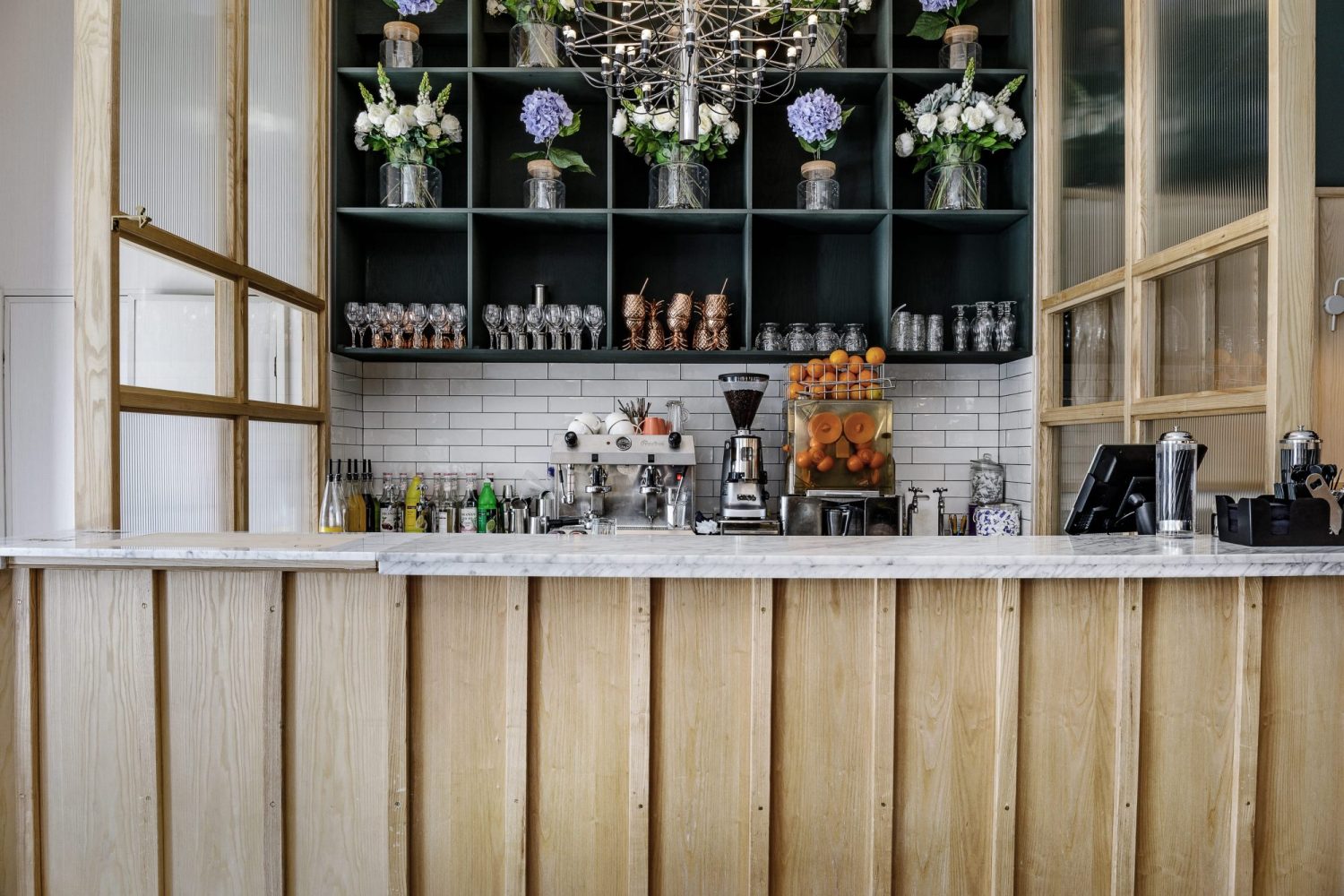 Restaurant bar with wooden counter and floral arrangements on shelves behind