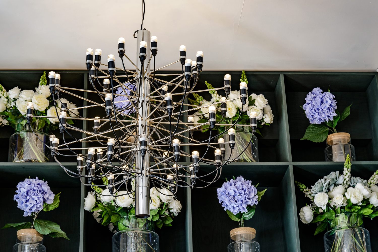 Close up on hanging chandelier with white and purple flowers on shelving behind