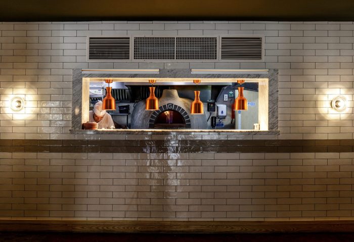 Restaurant food pass with copper heat lamps and pizza oven in background