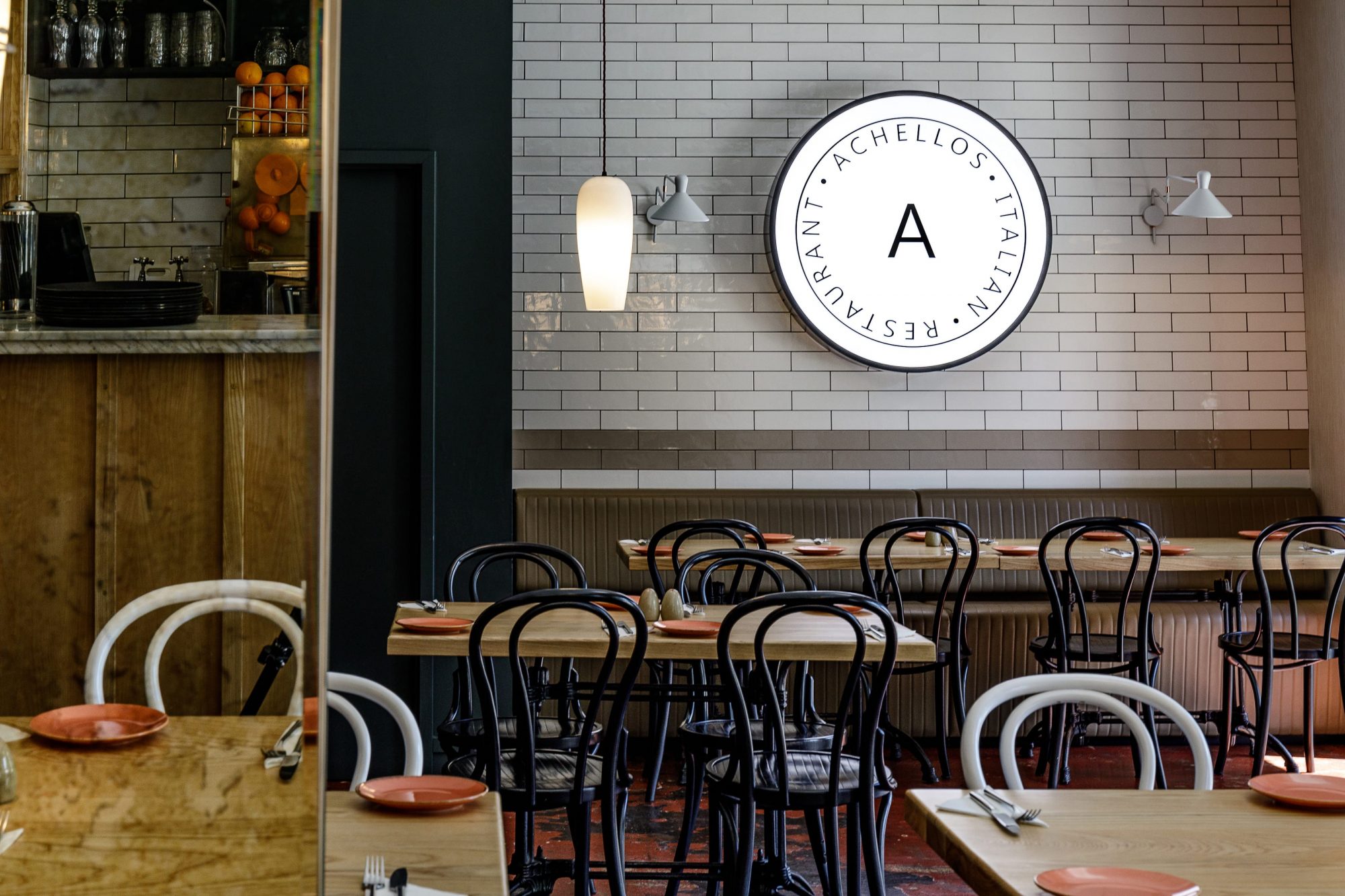 Achellos Italian Restaurant sign on white tiled wall with seating area below