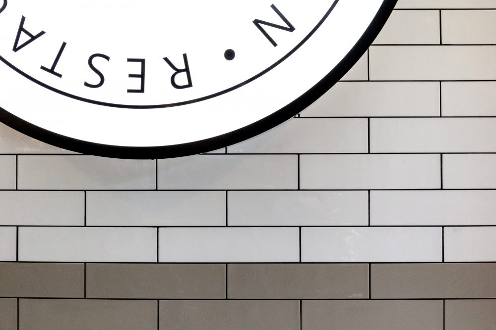 Edge of restaurant sign on white and grey tiled wall