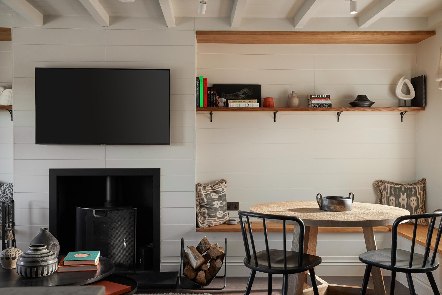 Living room with media wall featuring large TV above log burner with a long shelf to the side and circular wooden table with two black chairs