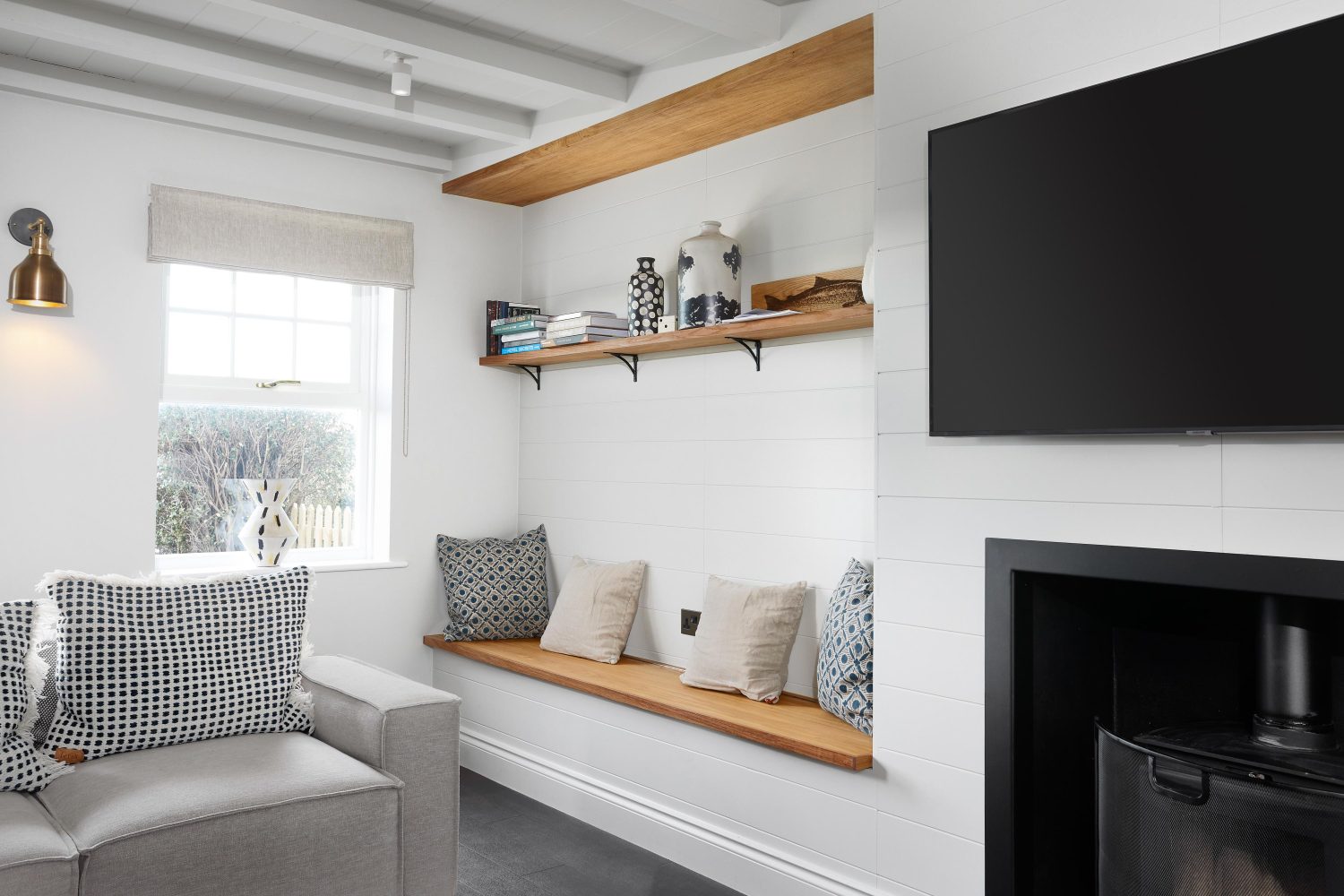 Media wall with Large TV above log burner and long shelf to the side with build in bench below with cushions