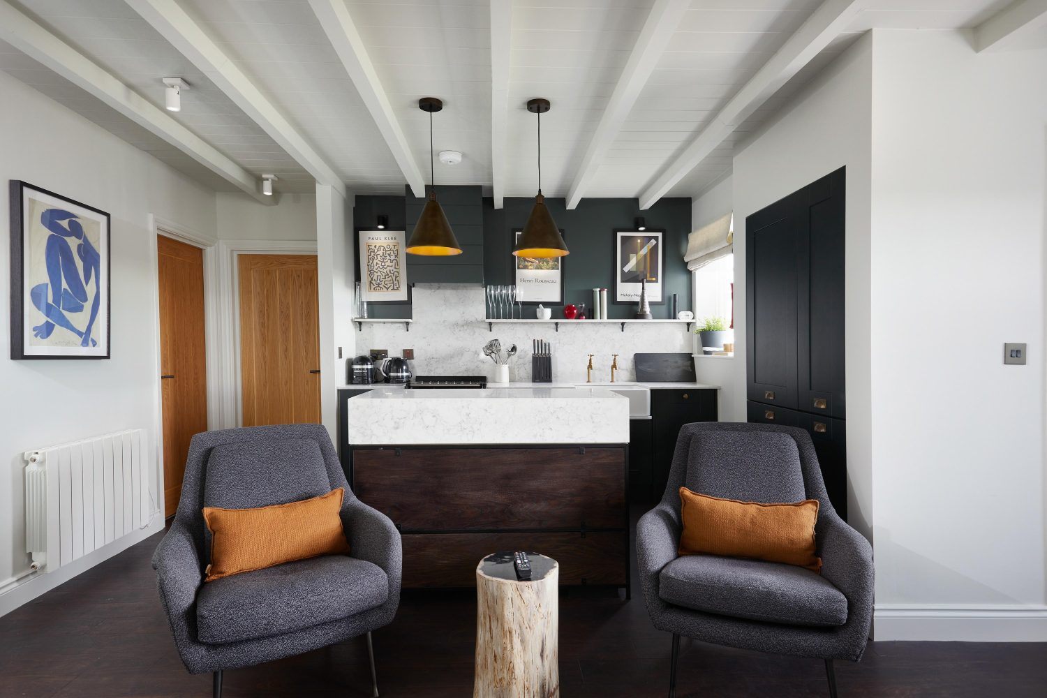 Kitchen with island in centre with two dark grey chairs in front and muted orange cushions