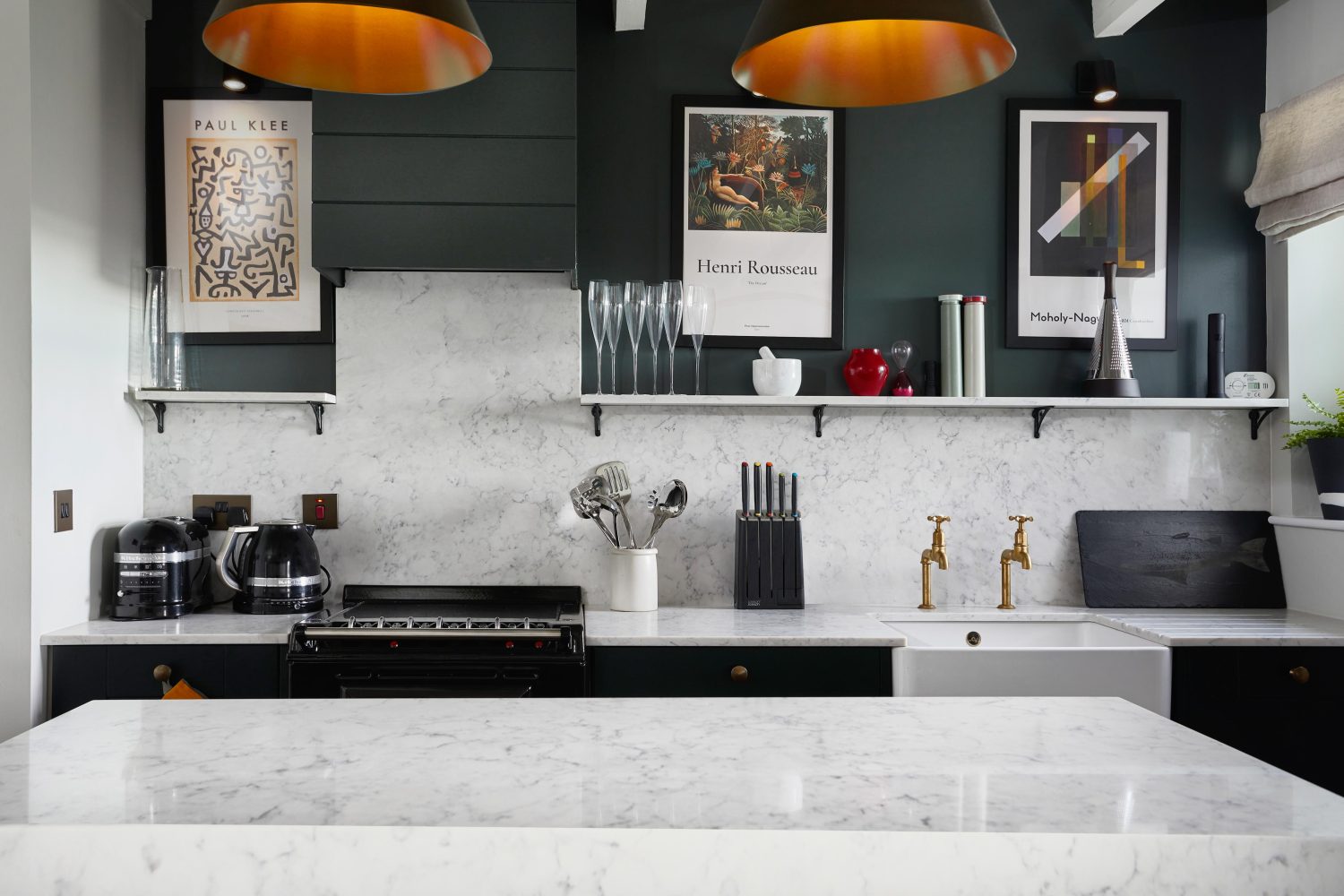Kitchen with dark grey walls and white marble countertops and backsplash with appliances on top and framed artwork on wall above