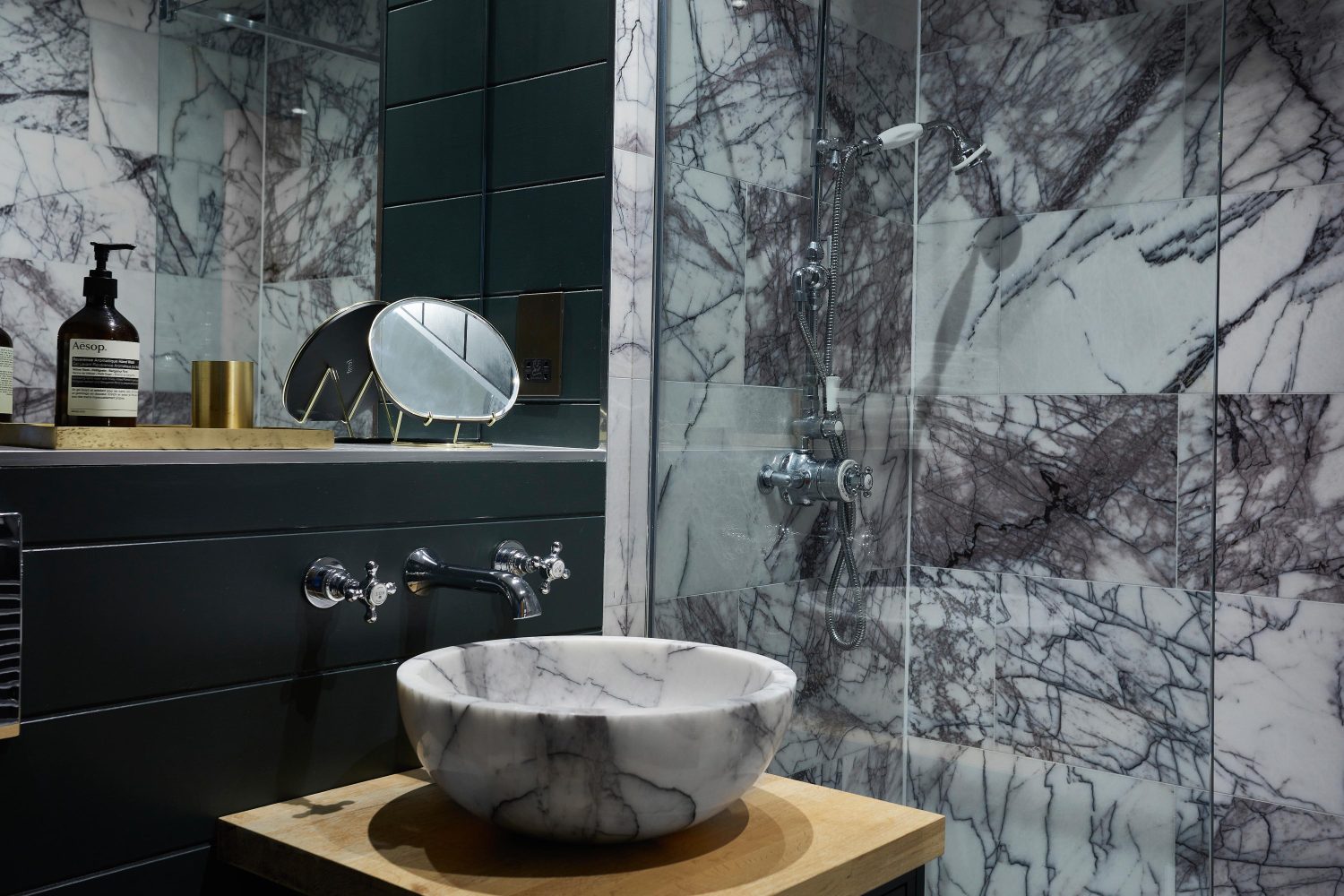 Bathroom with white and dark grey tiled shower with dark panelled walls and circular marble sink