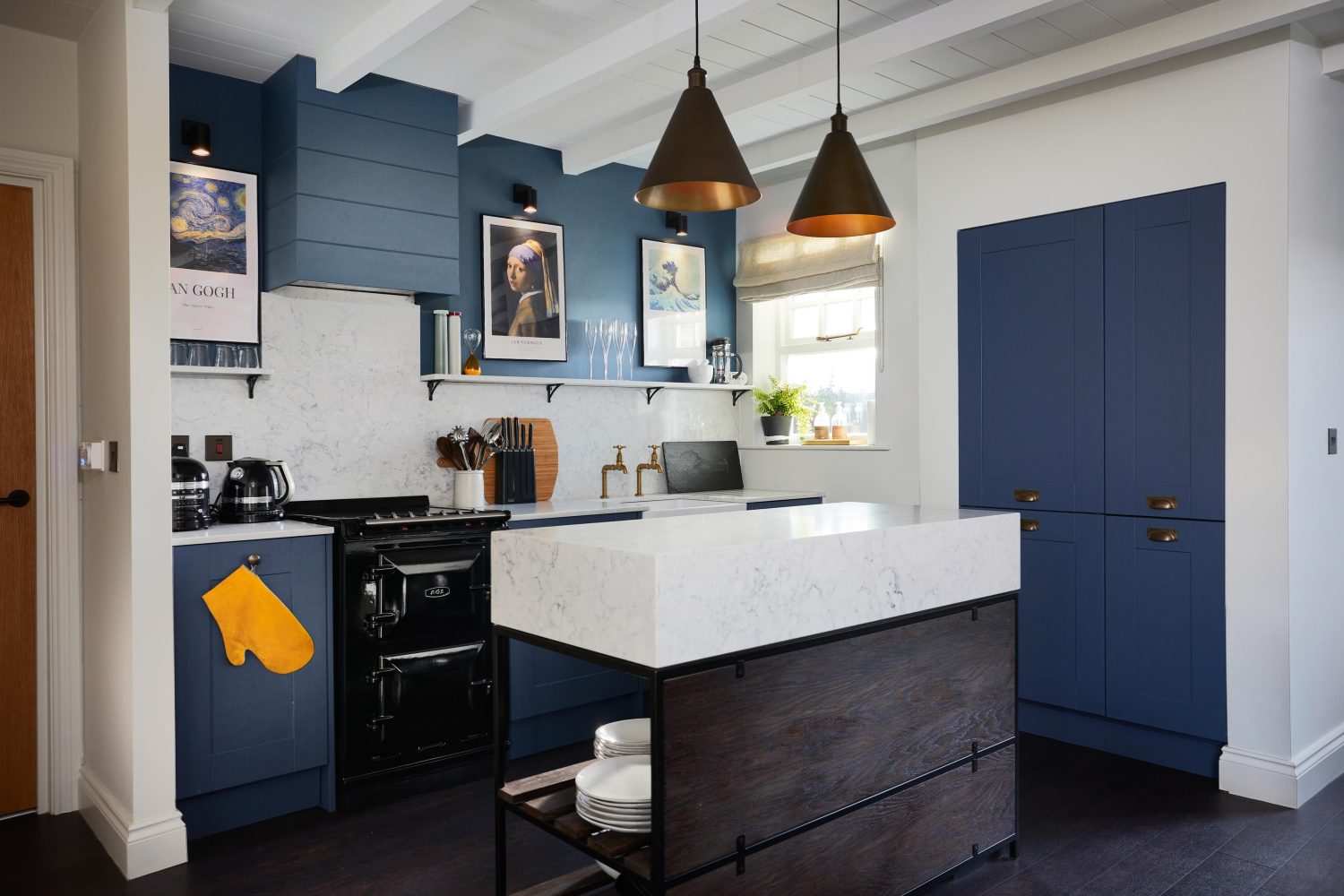Kitchen with muted blue cabinets and island in the centre with white marble countertop and two cone shaped pendant lights hanging from ceiling