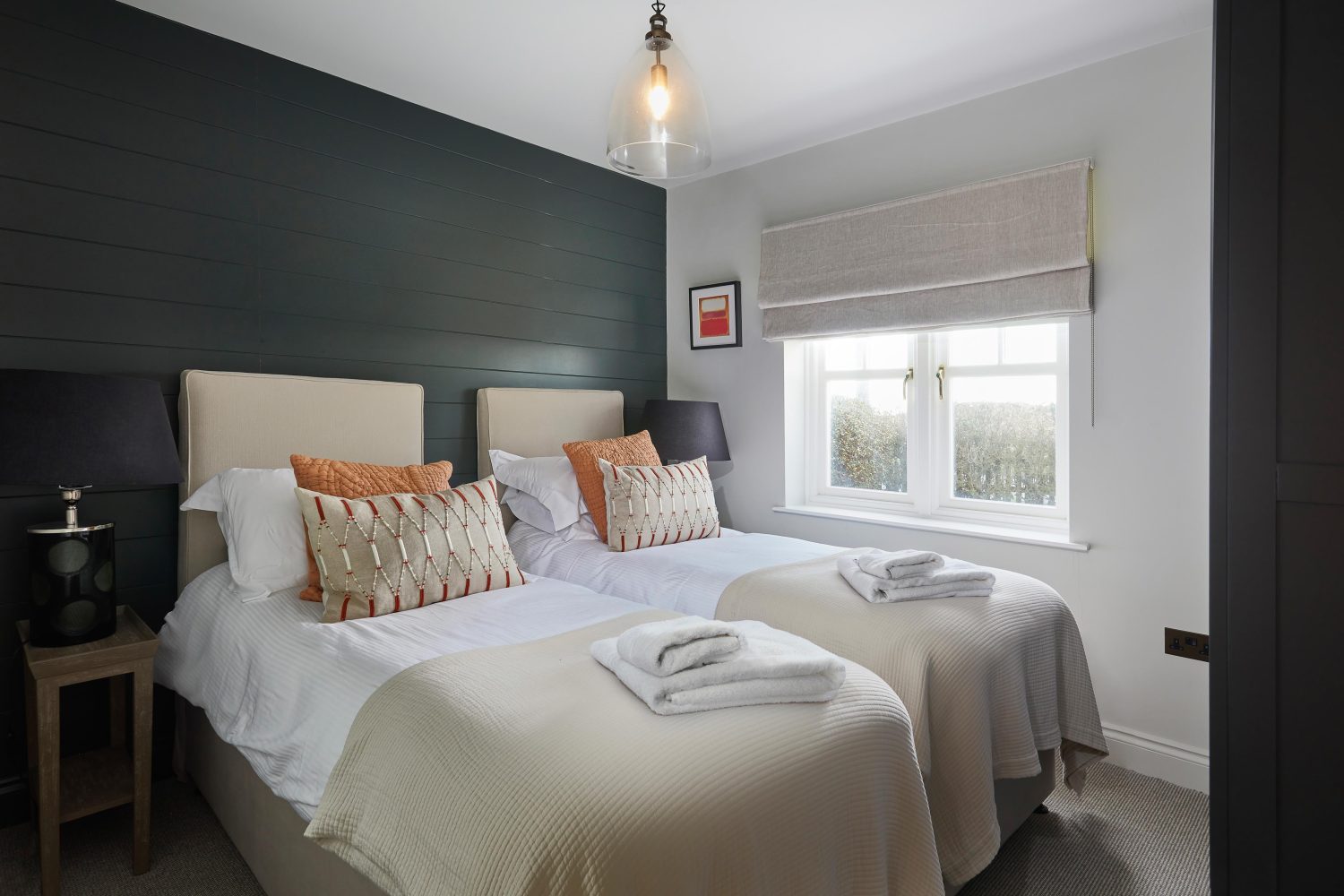 Bedroom with two single beds with dark green panelled wall behind and white double window to the side