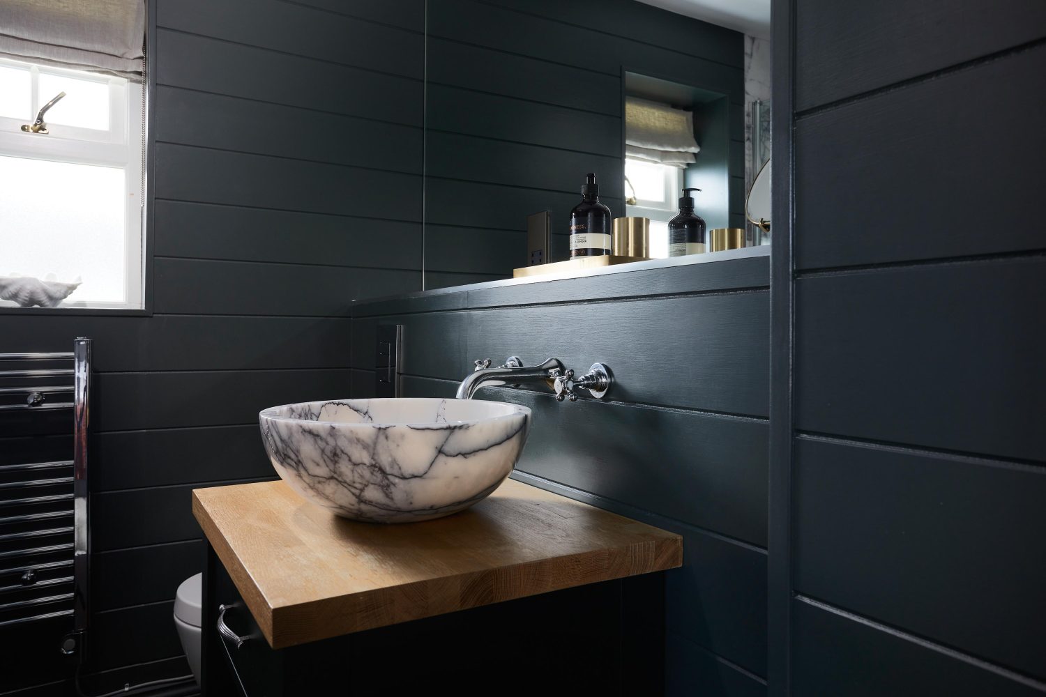 Bathroom with dark panelled walls and circular white and dark grey marble sink on top of wooden countertop with large mirror above
