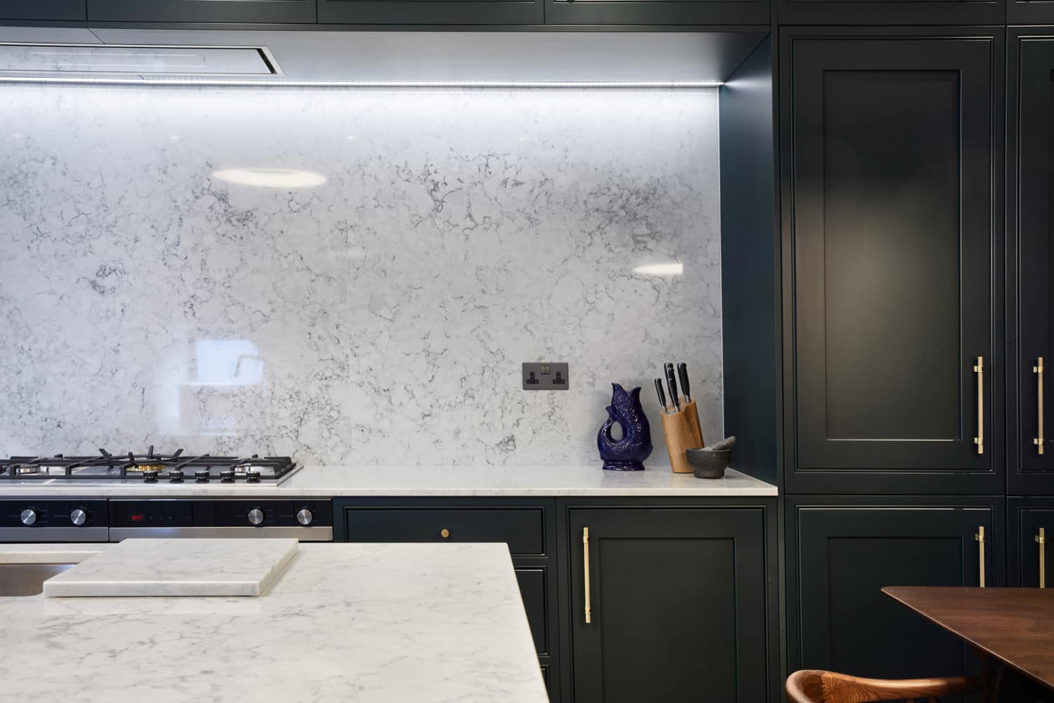 Kitchen with dark cabinetry and while marble countertops and back splash