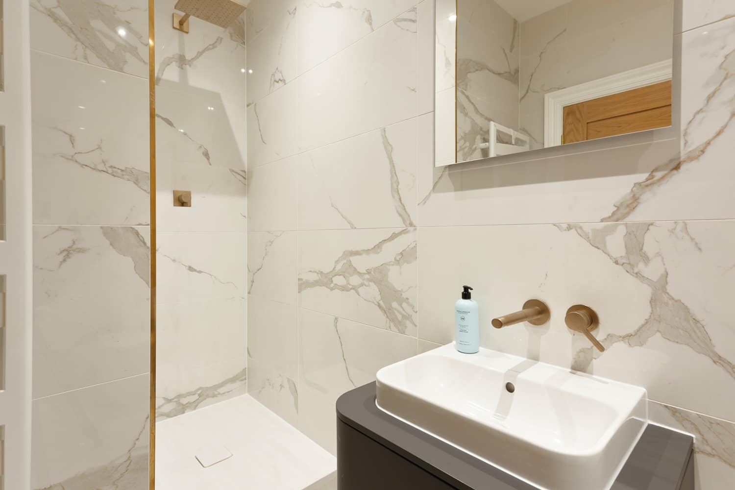 White marble bathroom with golden faucets and grey sink unit