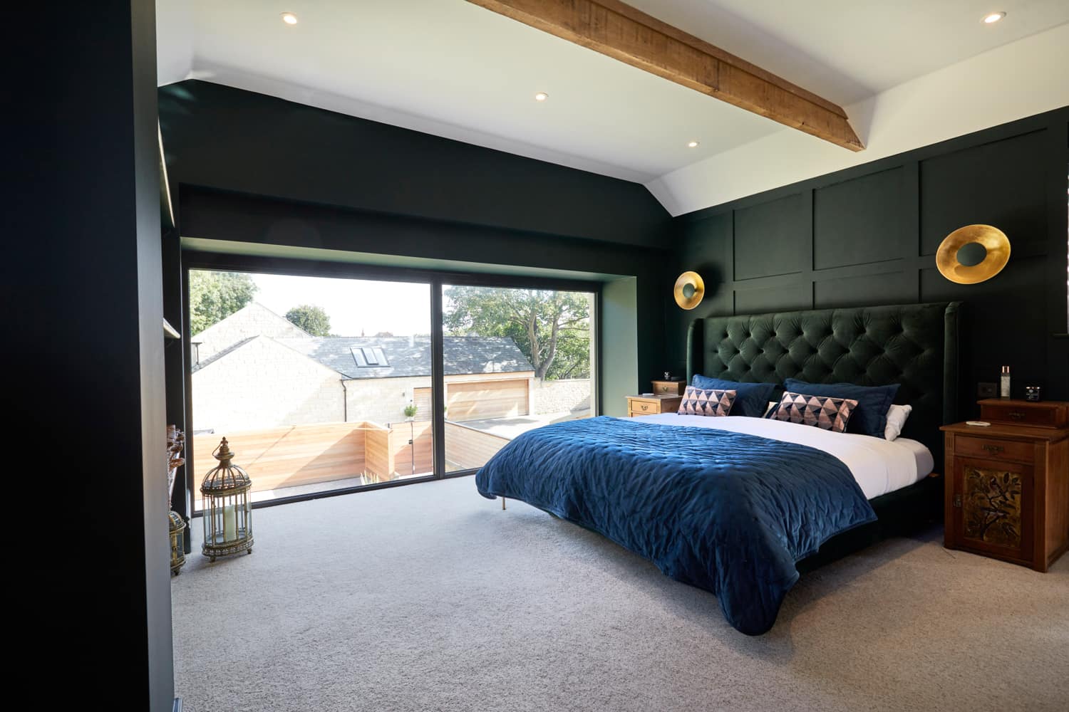 Bedroom with dark green walls and dark green cushioned headboard framed by large gold wall lamps