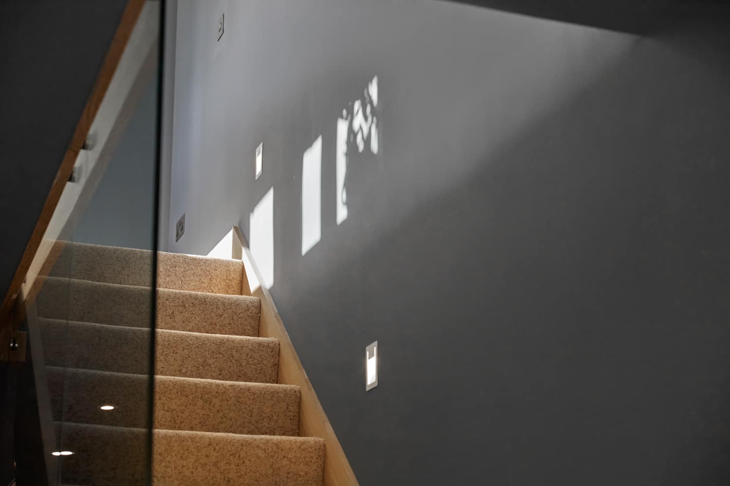 Top of carpeted staircase close up with glass barrier and muted blue walls